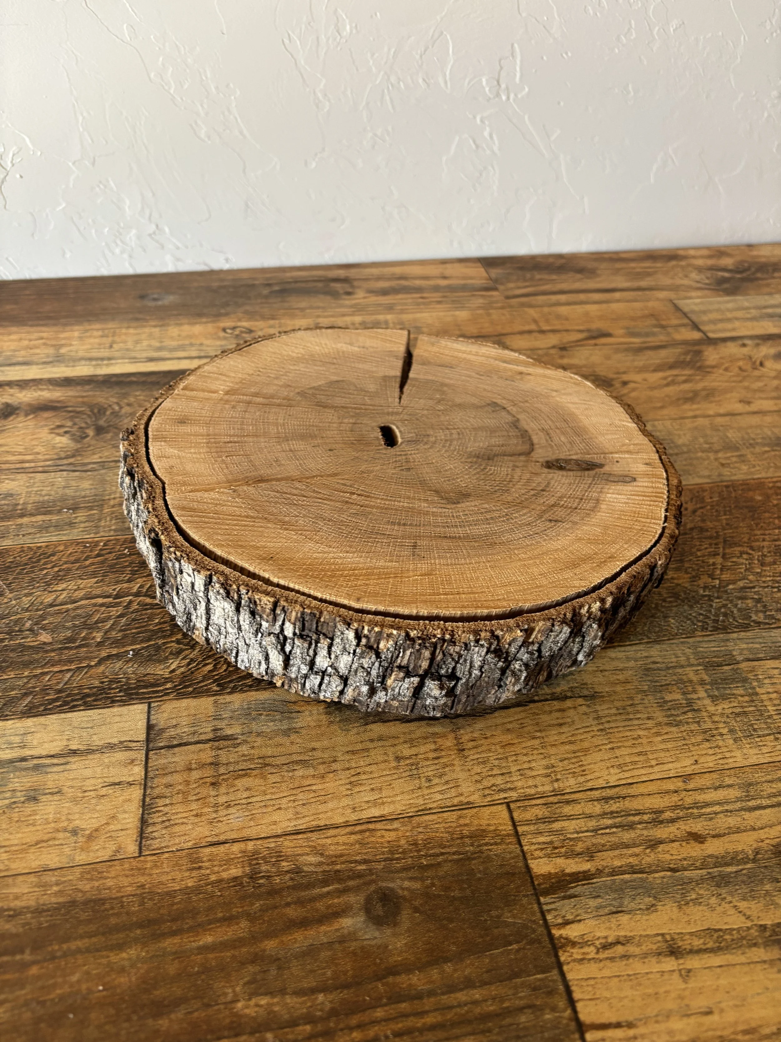 A round wooden cross-section with bark on the edges, placed on a wooden table.