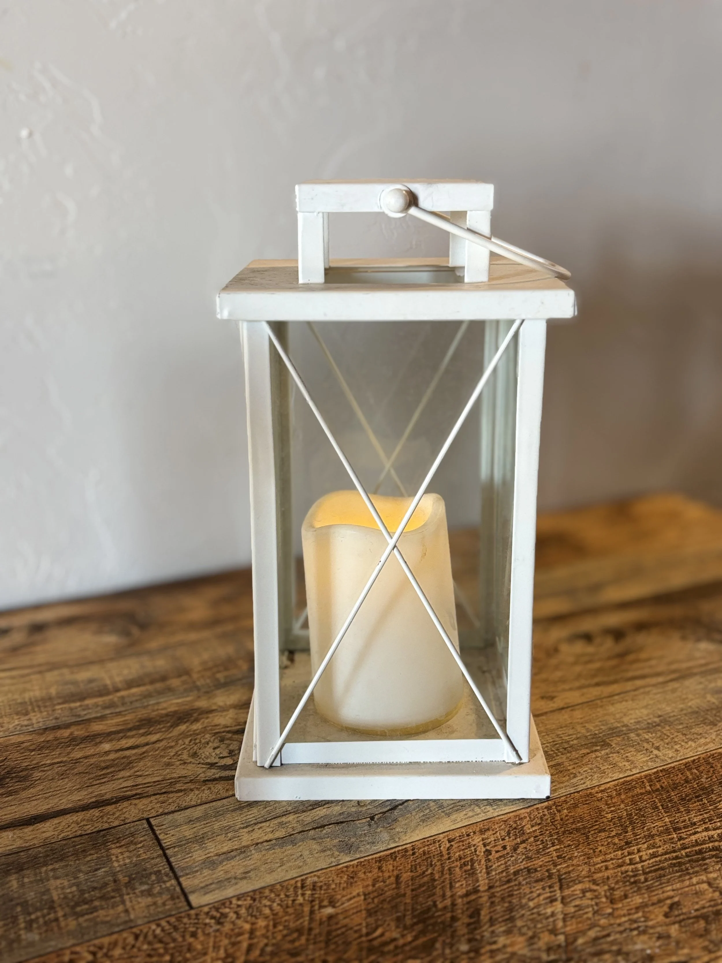 White lantern with a flickering candle inside, placed on a wooden surface.