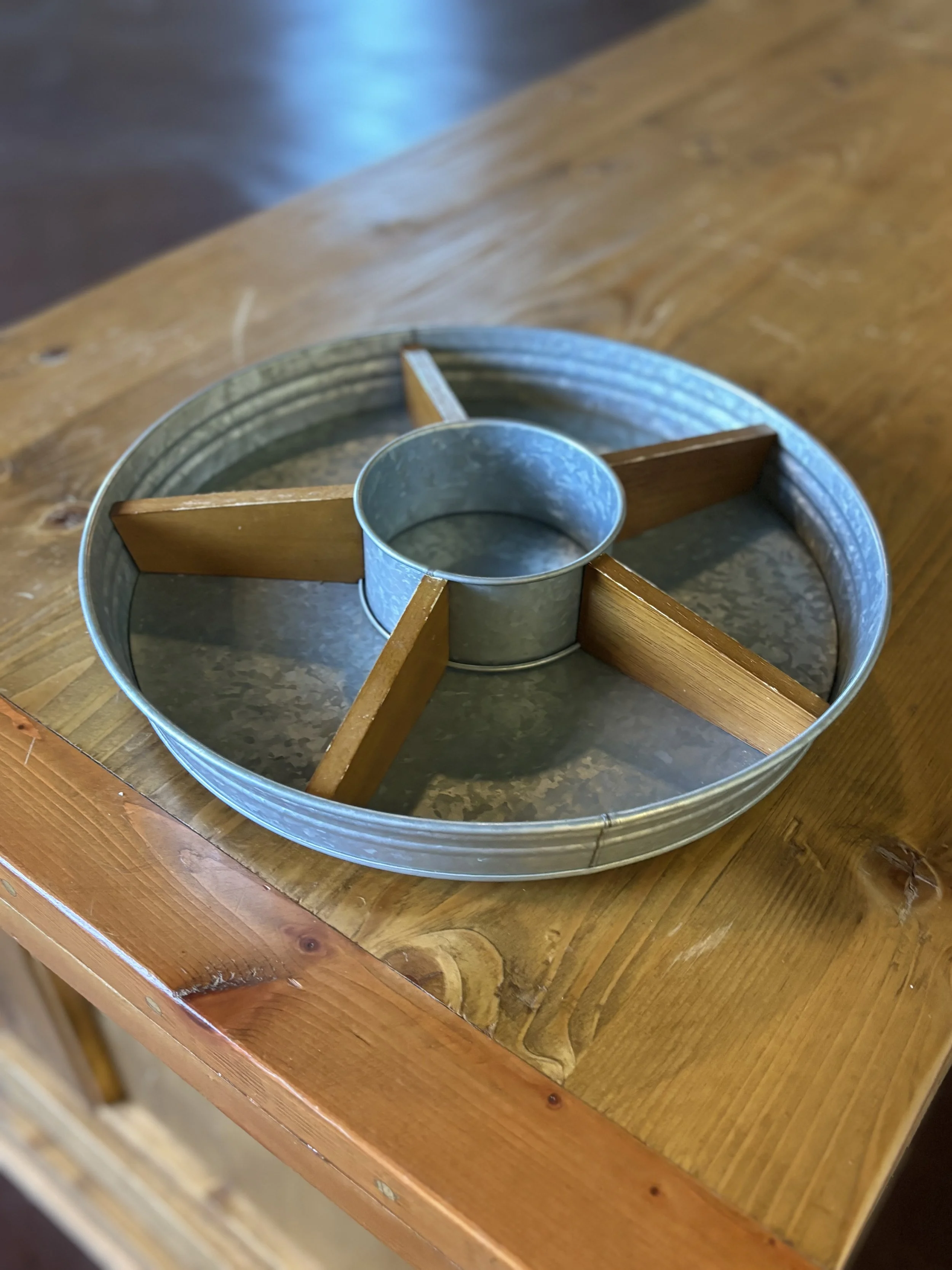 A round metal bingo or game wheel with wooden dividers on a wooden table.