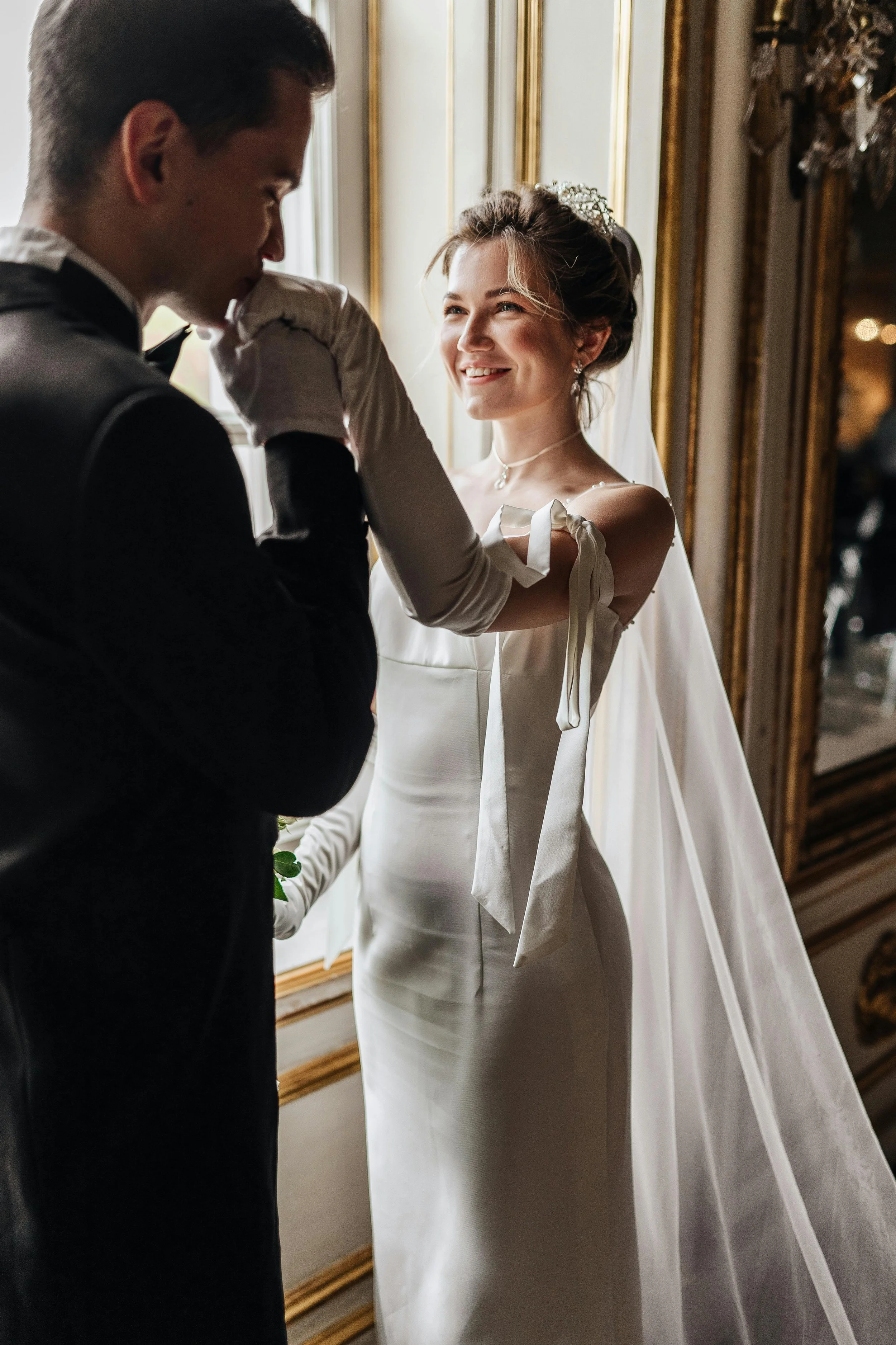 A bride and groom in Virginia Beach in wedding attire sharing a tender moment by a window in an elegant room.