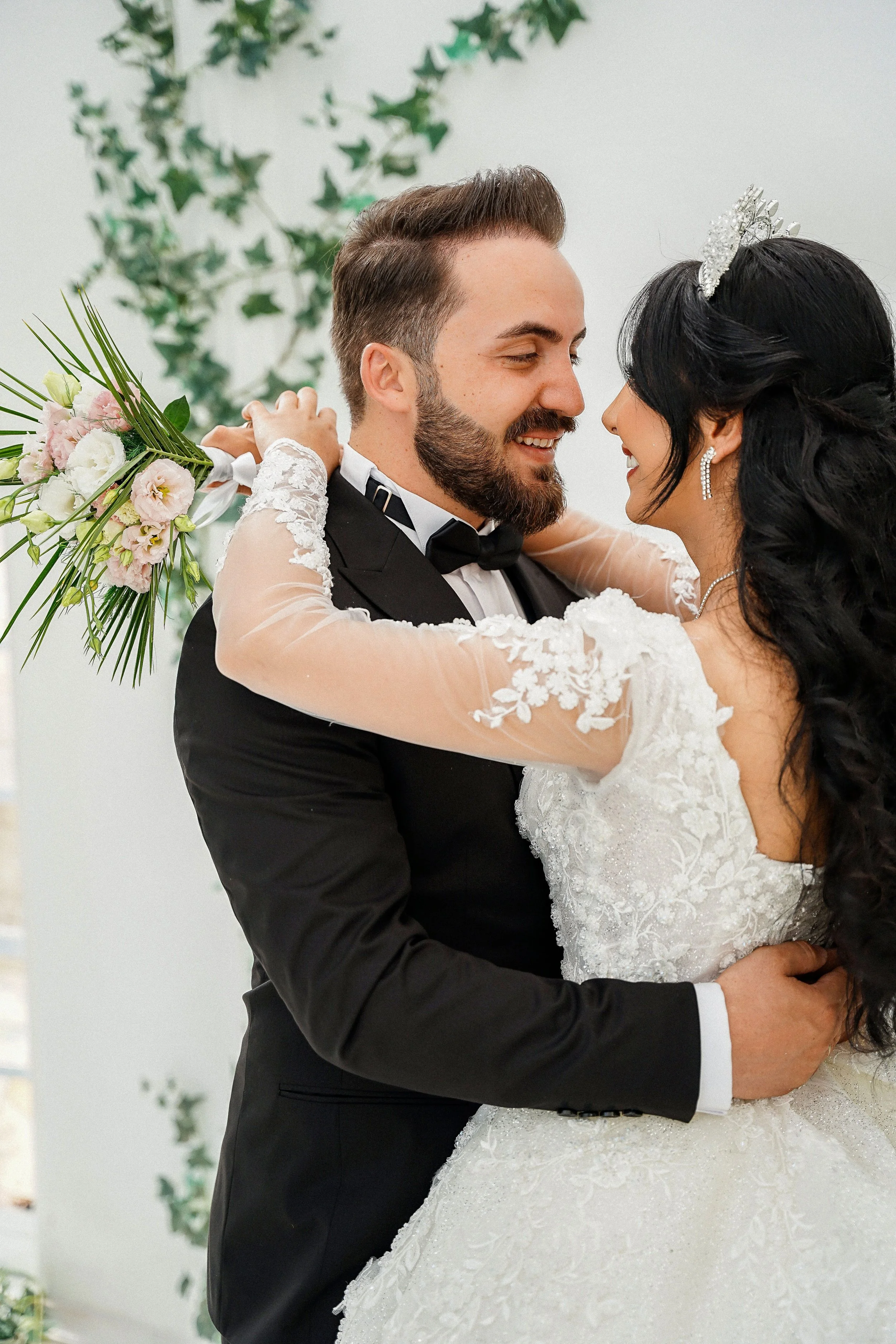 A virginia beach couple in wedding attire looking at each other. The bride has her arms wrapped around the groom's neck and is holding flowers