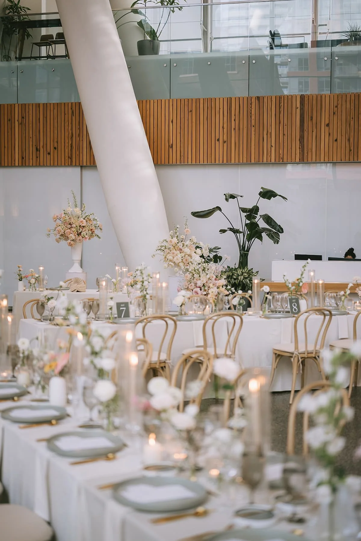 Wide view of the reception at Ricarda's Toronto showcasing soft neutral floral arrangements, candlelit tablescapes, bentwood chairs, and a modern minimalist wedding design.