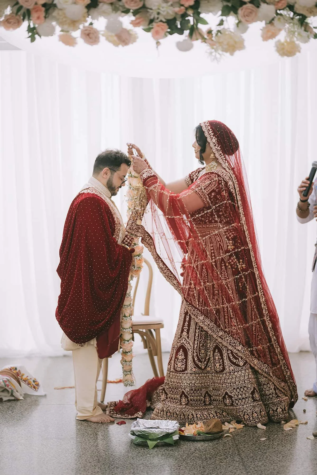 Bride placing a floral garland around the groom's neck during the Jaimala ceremony at a Hindu wedding at Ricarda's in Toronto.