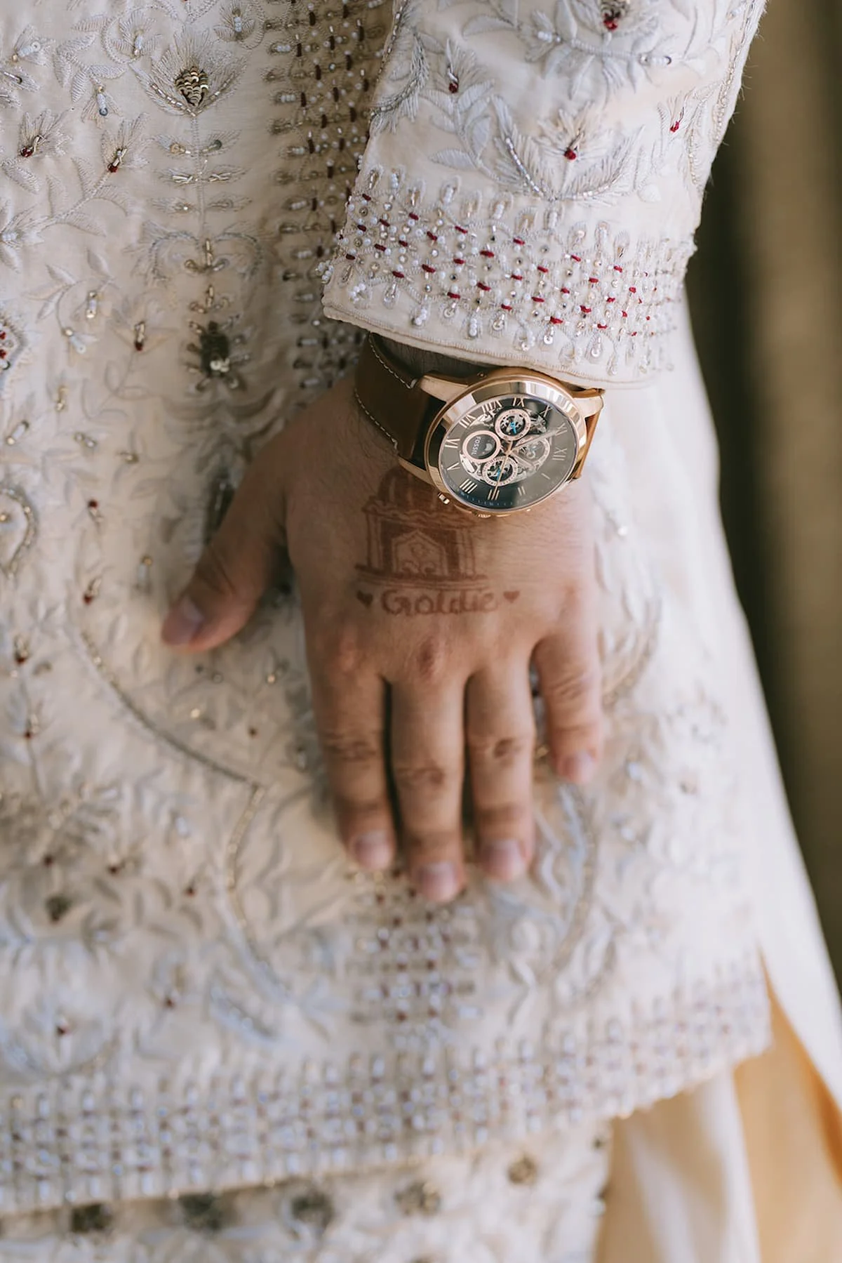 Close-up of an embroidered ivory sherwani with the groom's watch and personalized mehndi before a modern Hindu wedding in Toronto.