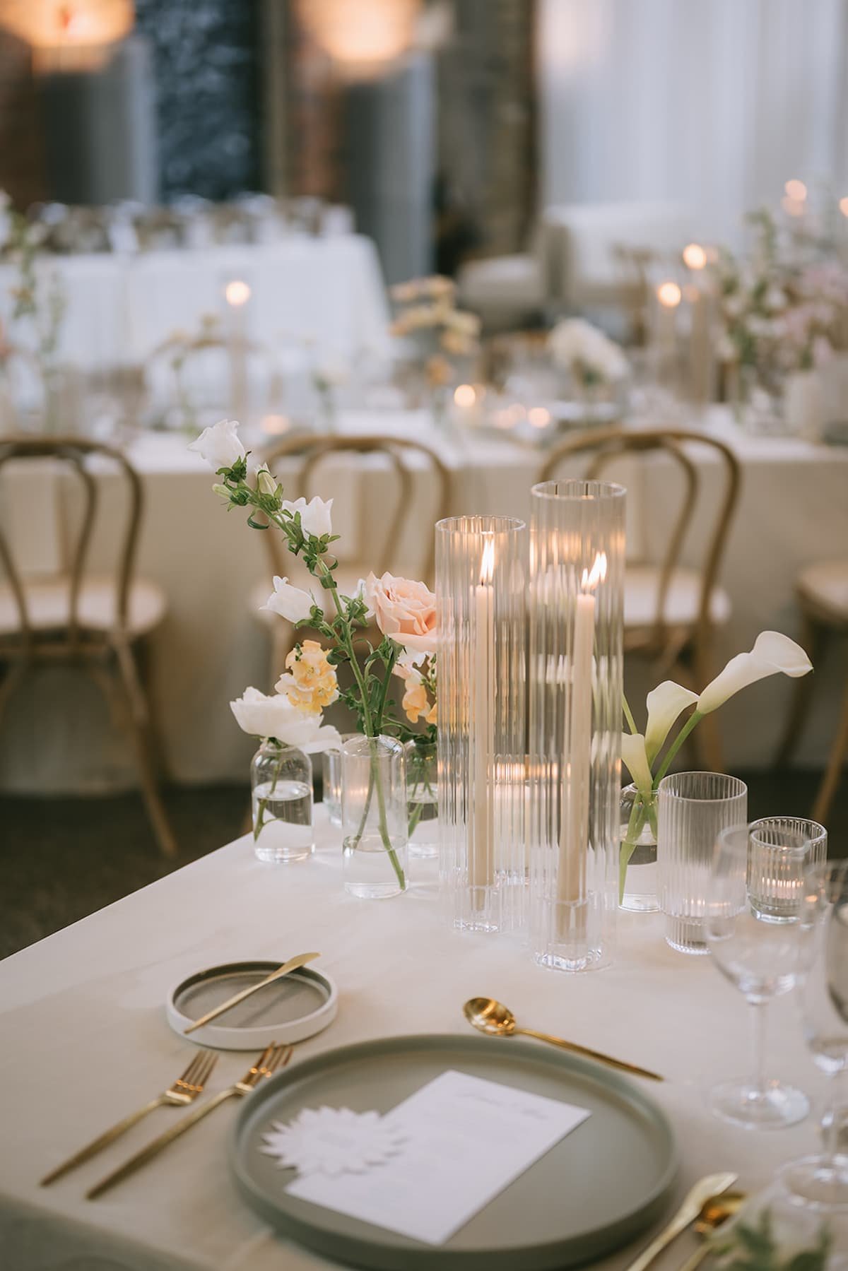 Minimalist wedding reception centrepiece with bud vases, blush and white florals, ribbed glass taper candle holders, and modern place settings at Ricarda's Toronto.