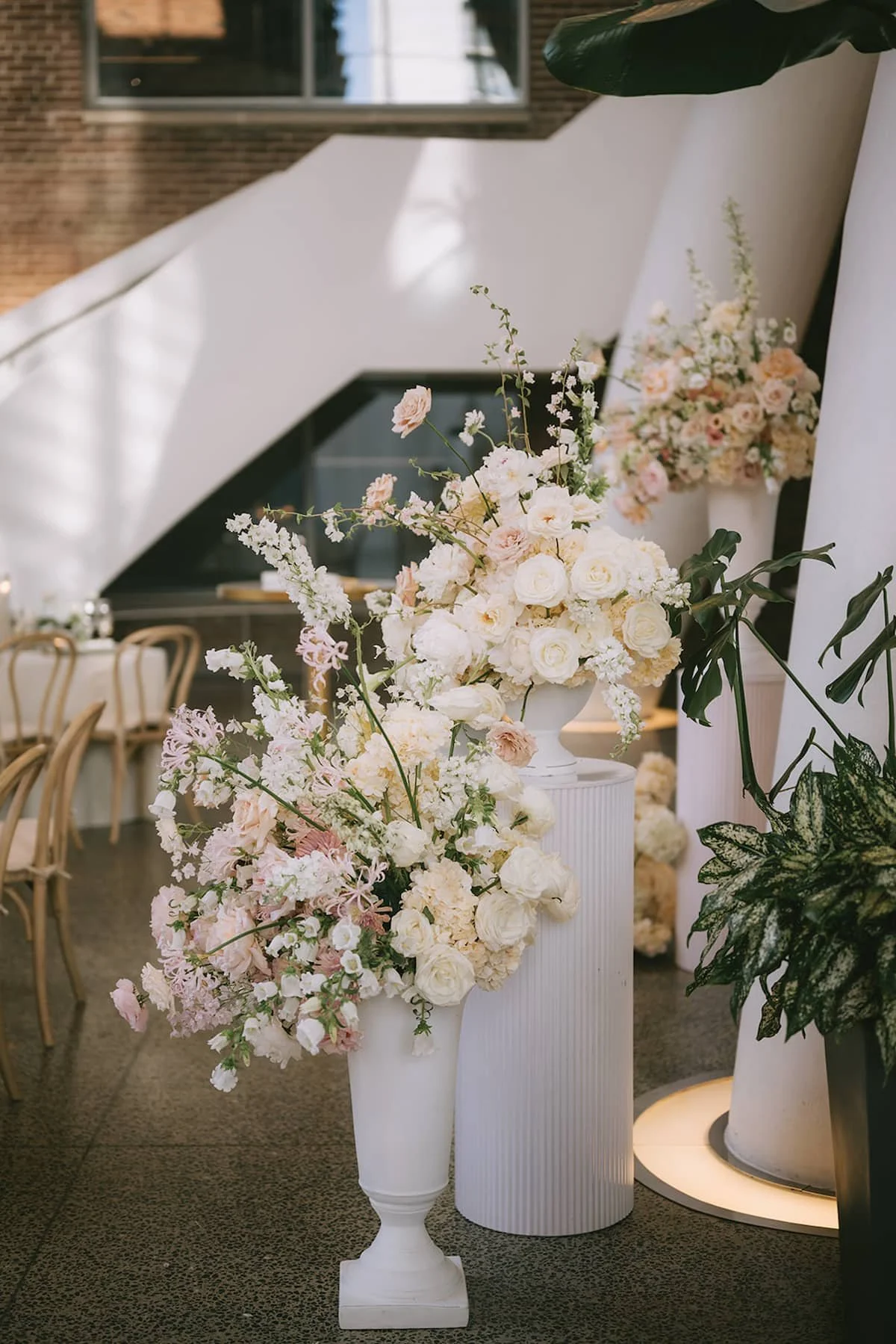 Asymmetrical floral installation in white urns and pedestal vessels featuring white and blush flowers at a luxury Hindu wedding reception at Ricarda's Toronto.