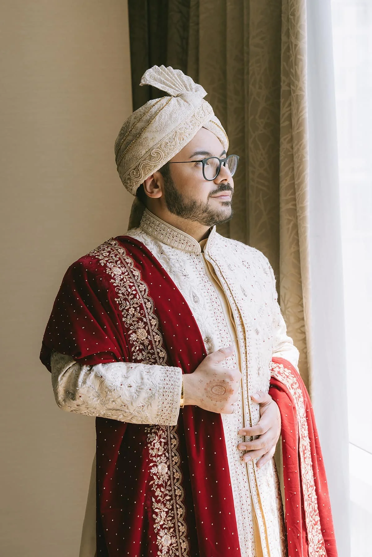 Portrait of a groom wearing an ivory embroidered sherwani, traditional turban, and red shawl before a modern Hindu wedding ceremony in Toronto.