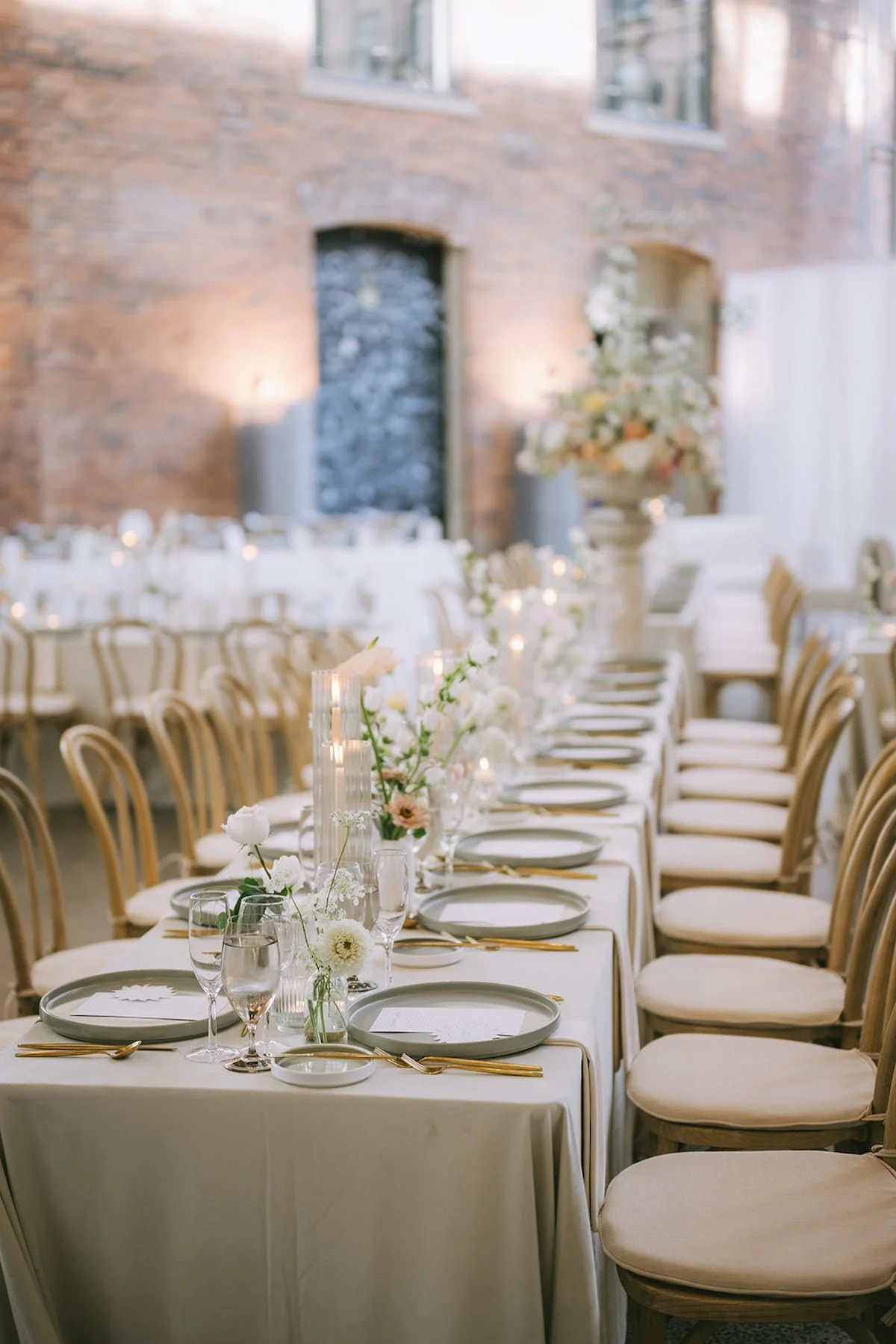 Long reception table at Ricarda's in Toronto featuring neutral linens, bud vase florals, candlelight, gold flatware, and minimalist place settings for a luxury Hindu wedding.