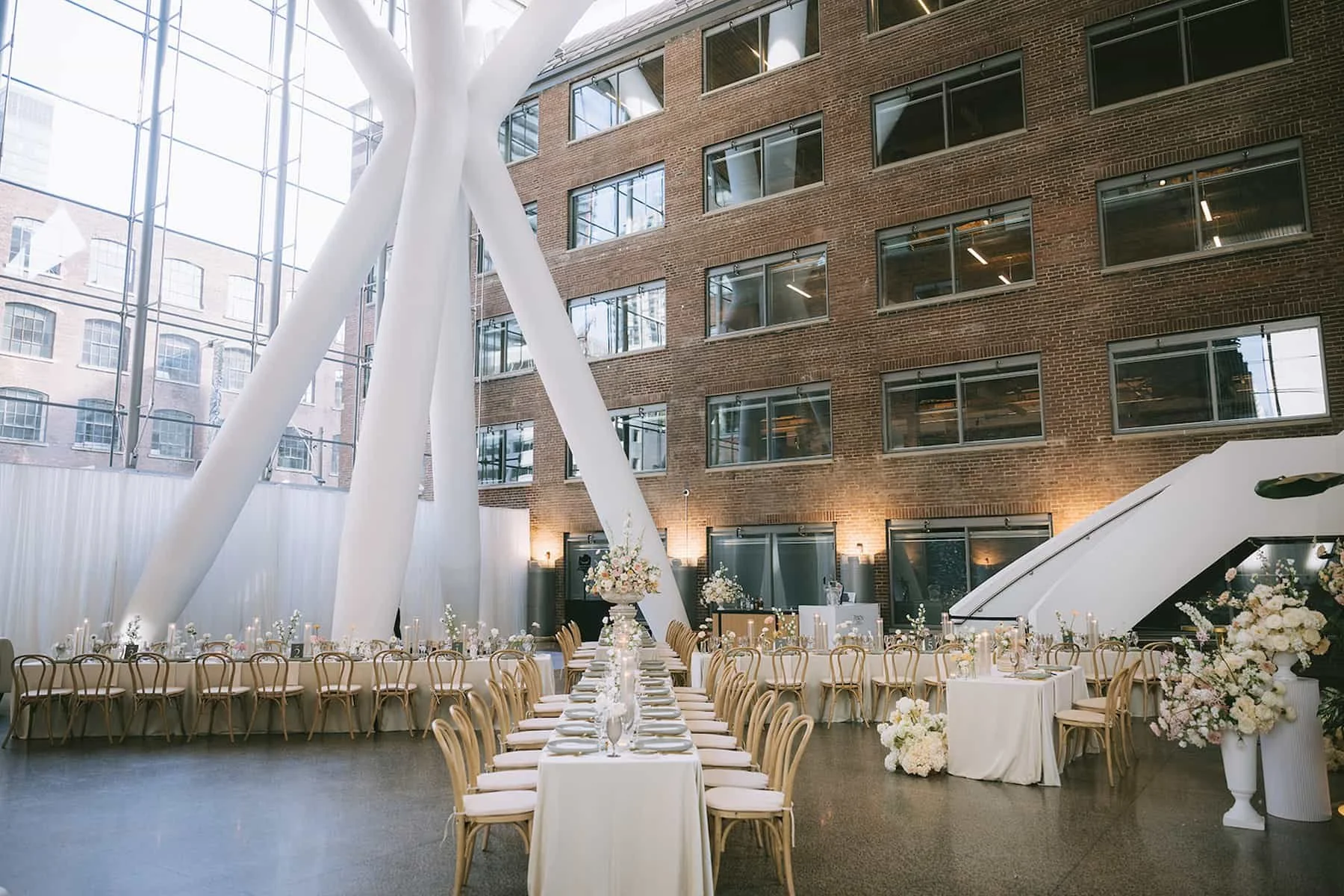 Wide view of the wedding reception design at Ricarda's in Toronto featuring long guest tables, soft neutral florals, candlelight, and floor-to-ceiling windows.