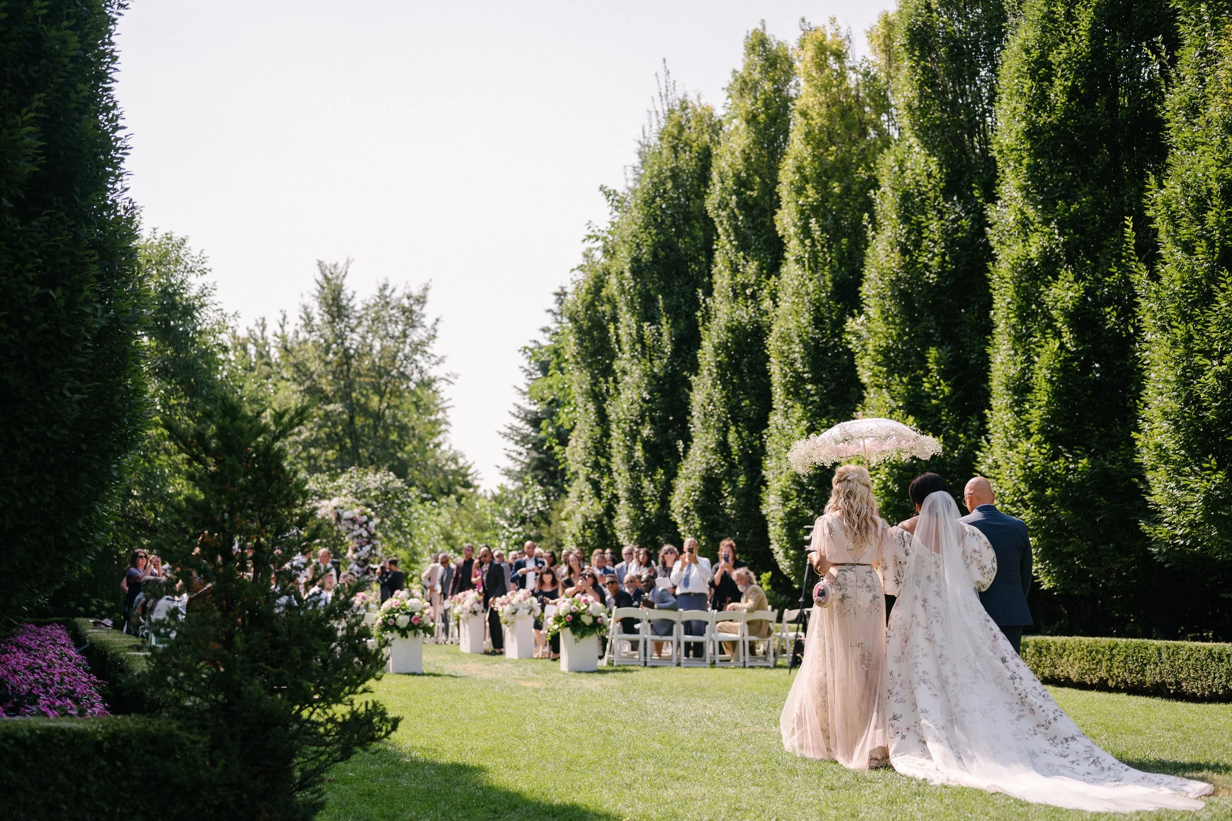 The ultimate luxury wedding experience at Graydon Hall Manor in Toronto as bride walks down the aisle with her parents in a floral wedding gown