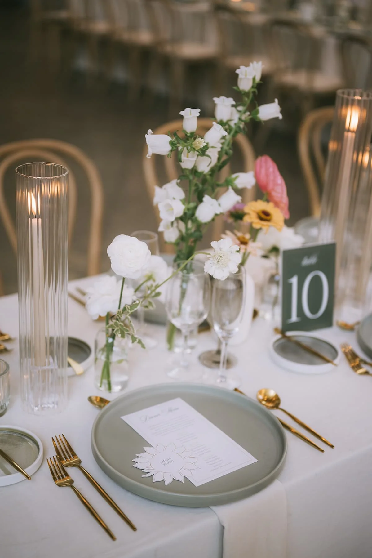 Modern wedding tablescape at Ricarda's Toronto featuring grey stoneware plates, gold flatware, ribbed glass candle holders, and colourful bud vase florals for a luxury Hindu wedding.