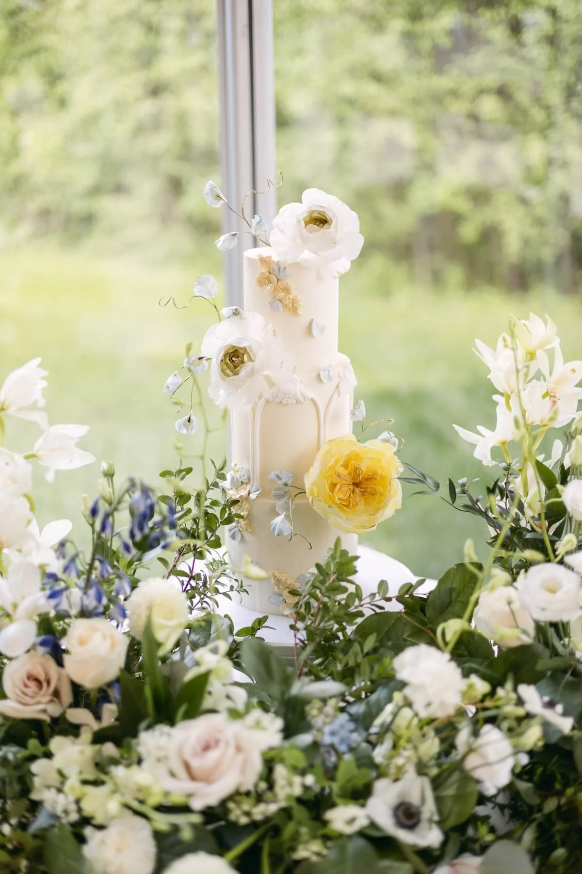 Modern white wedding cake surrounded by fresh garden flowers during a reception at Harding Waterfront Estate.