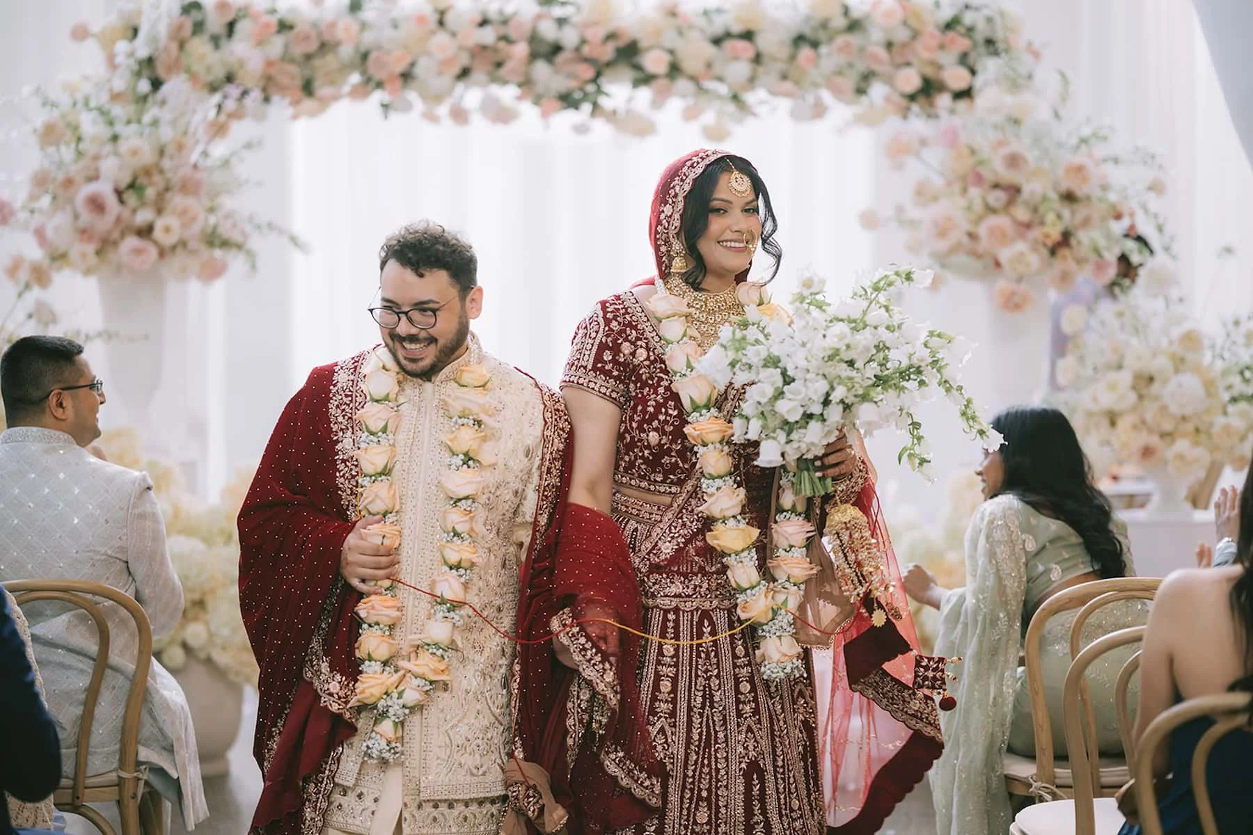 Bride and groom walking down the aisle after their Hindu wedding ceremony at Ricarda's in Toronto, surrounded by lush floral installations and natural light.