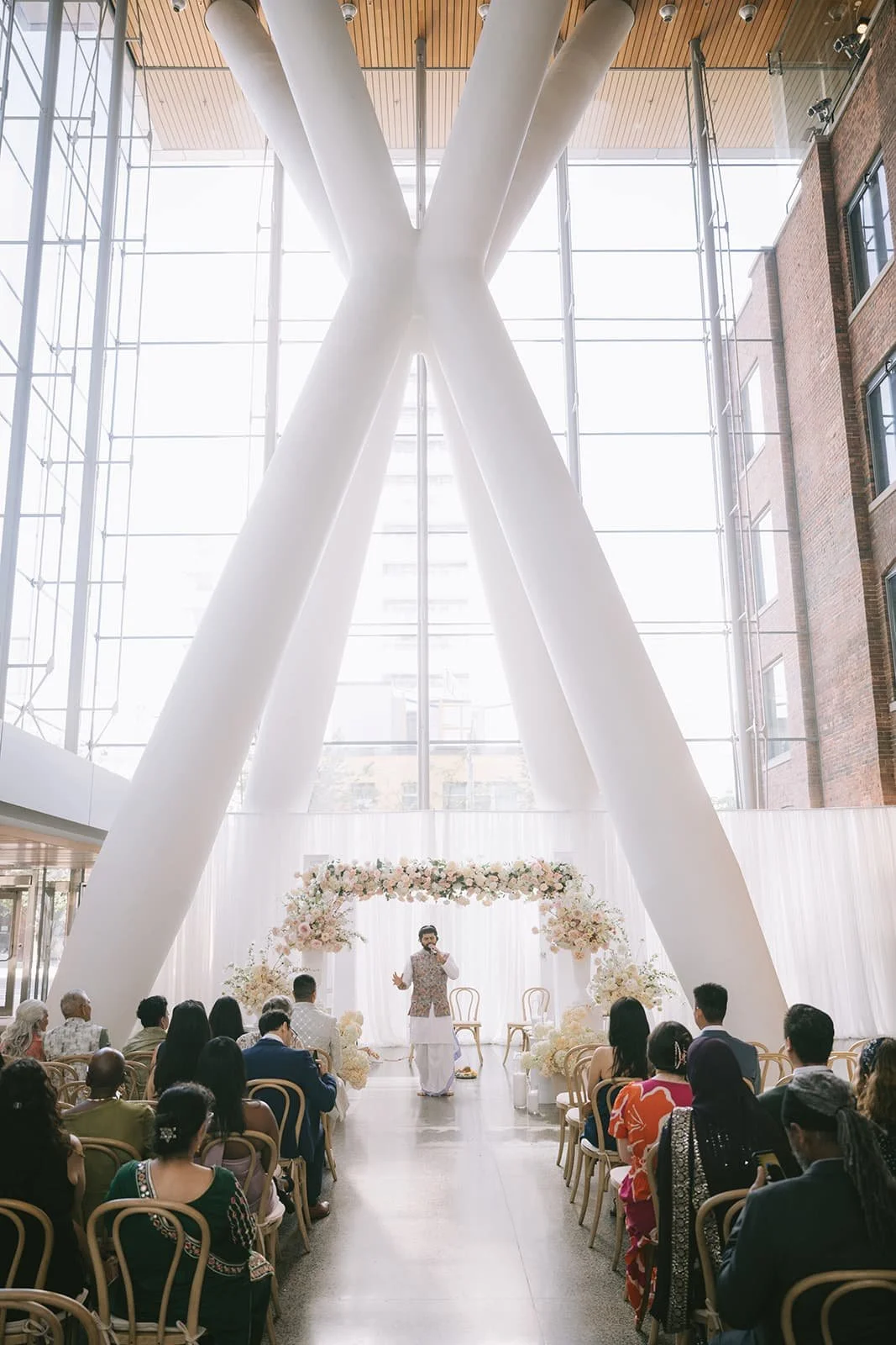 Wide view of a Hindu wedding ceremony at Ricarda's in Toronto featuring a floral mandap, floor-to-ceiling windows, and guests gathered for the ceremony.