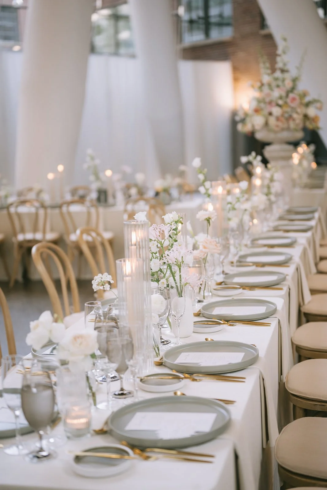 Long head table at a luxury Hindu wedding at Ricarda's Toronto featuring soft neutral florals, taper candles, grey stoneware plates, gold flatware, and a minimalist tablescape.