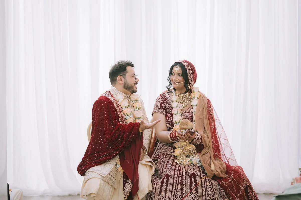 Bride and groom smiling during a Hindu wedding ceremony while holding a sacred coconut beneath a floral mandap at Ricarda's in Toronto.