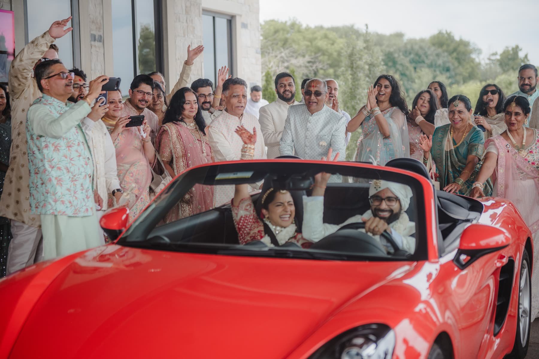 Ashika and Sagar celebrate their grand exit in a red convertible as family and friends cheer outside Arlington Estate following their Hindu wedding ceremony.