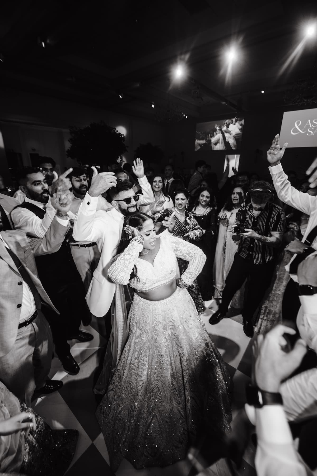 Bride and groom celebrating on a packed dance floor surrounded by family and friends during their luxury South Asian wedding reception at Arlington Estate.