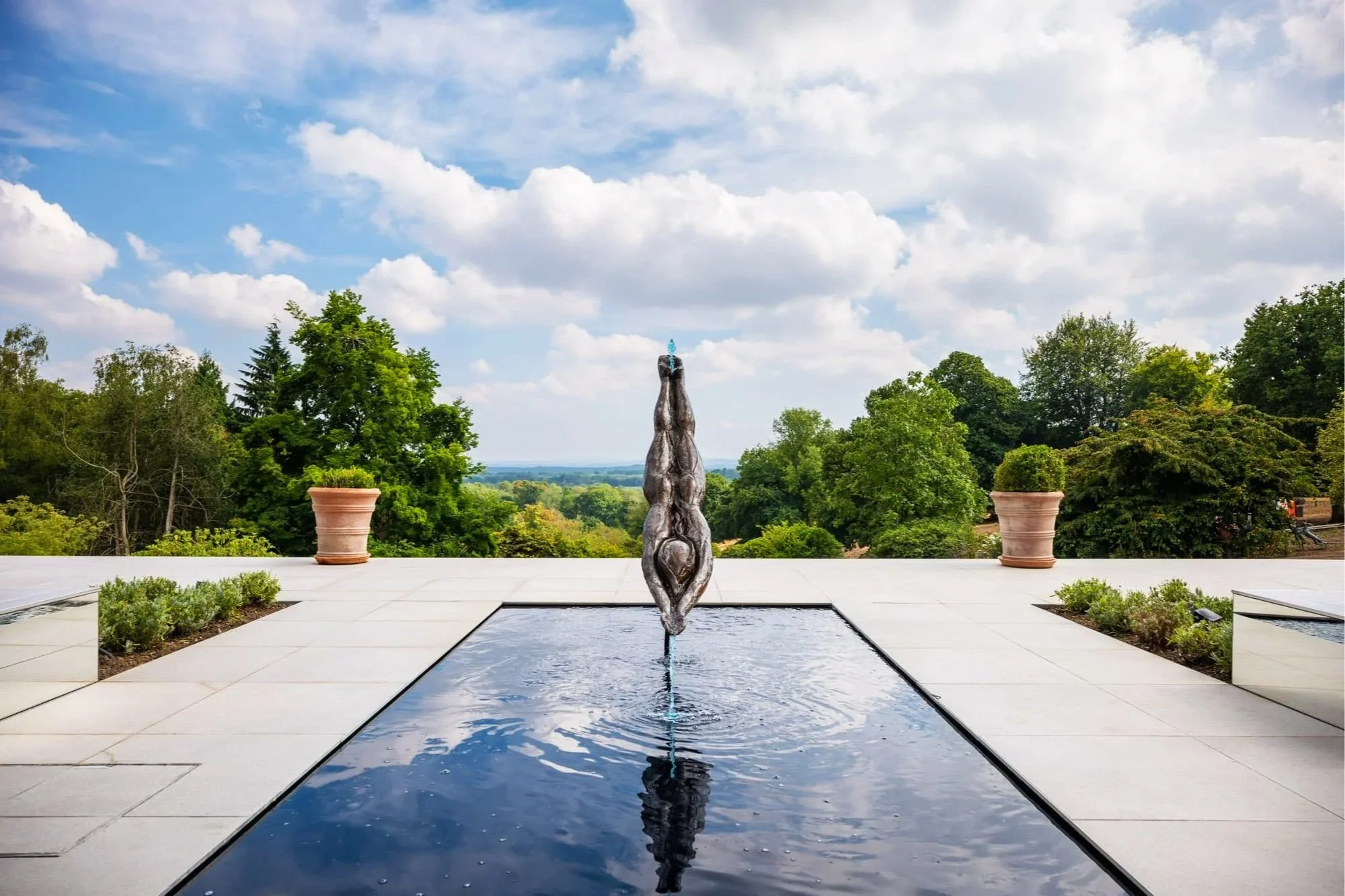 A modern fountain with a sculpture of two figures in a yoga pose, located in an outdoor space.