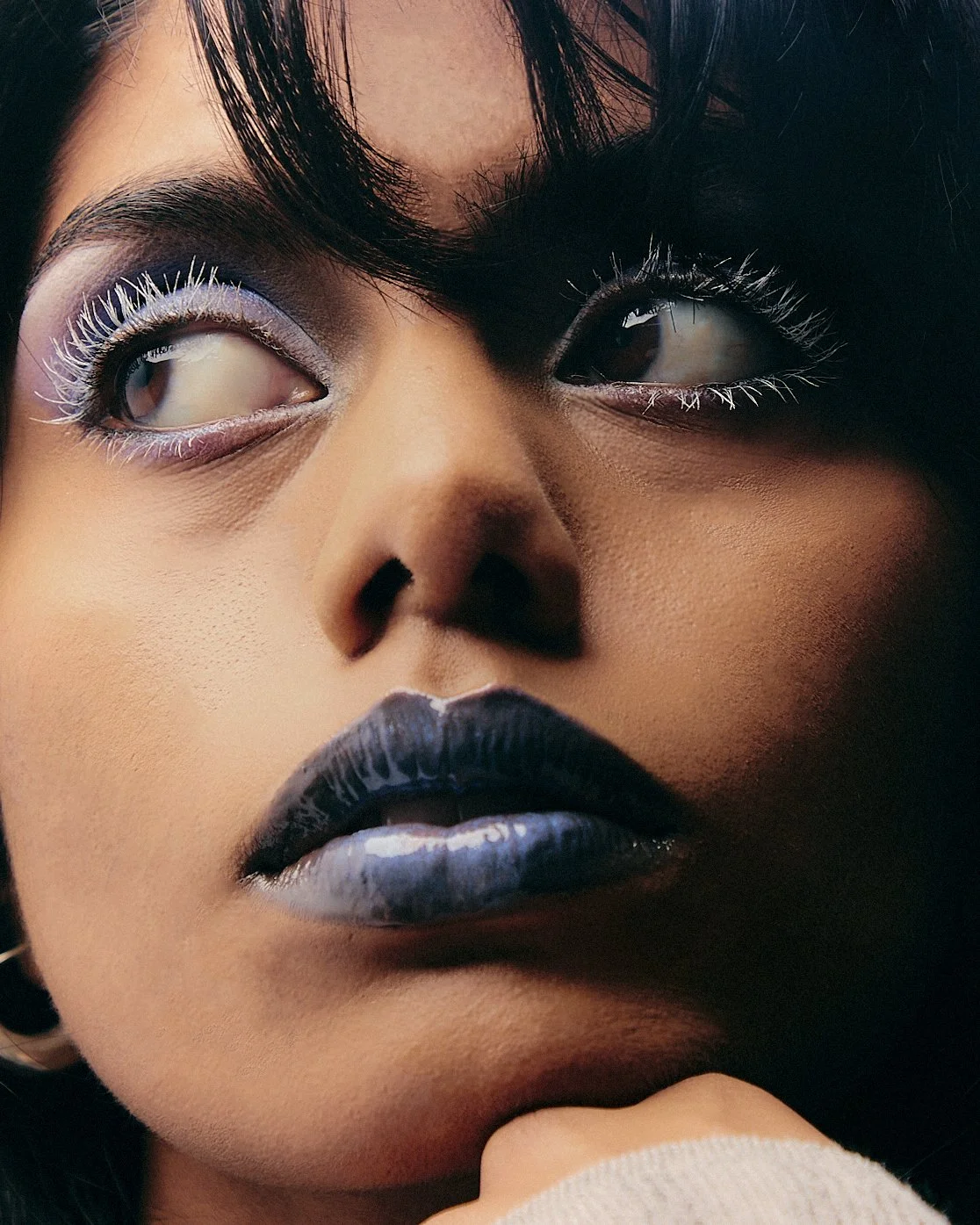 Close-up of a woman with bold makeup, including white eyeliner, dark lipstick, and styled hair.