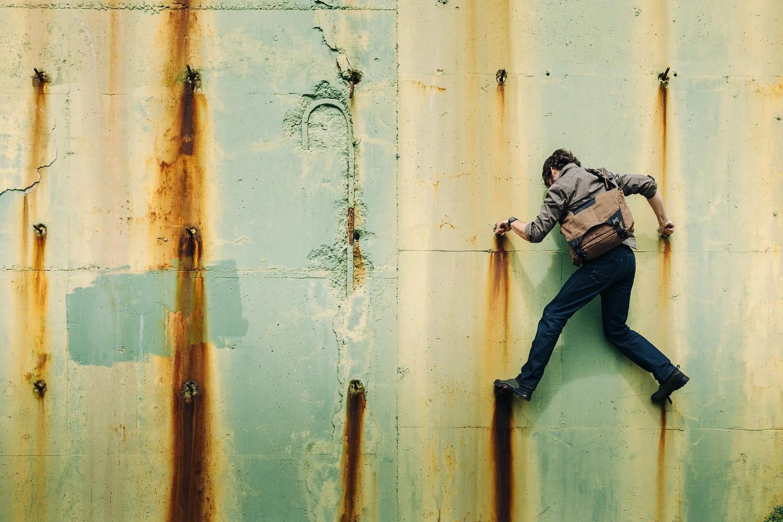 A person climbing a rusty, weathered metal wall with their hands and feet.