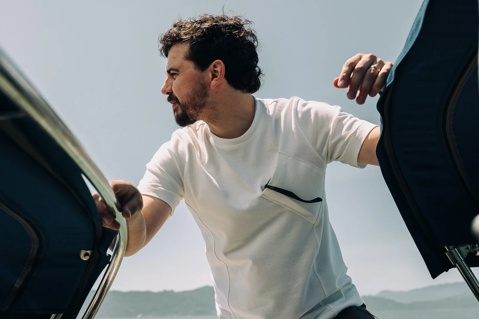 A man with dark, curly hair wearing a white t-shirt is seen loading luggage onto a boat.