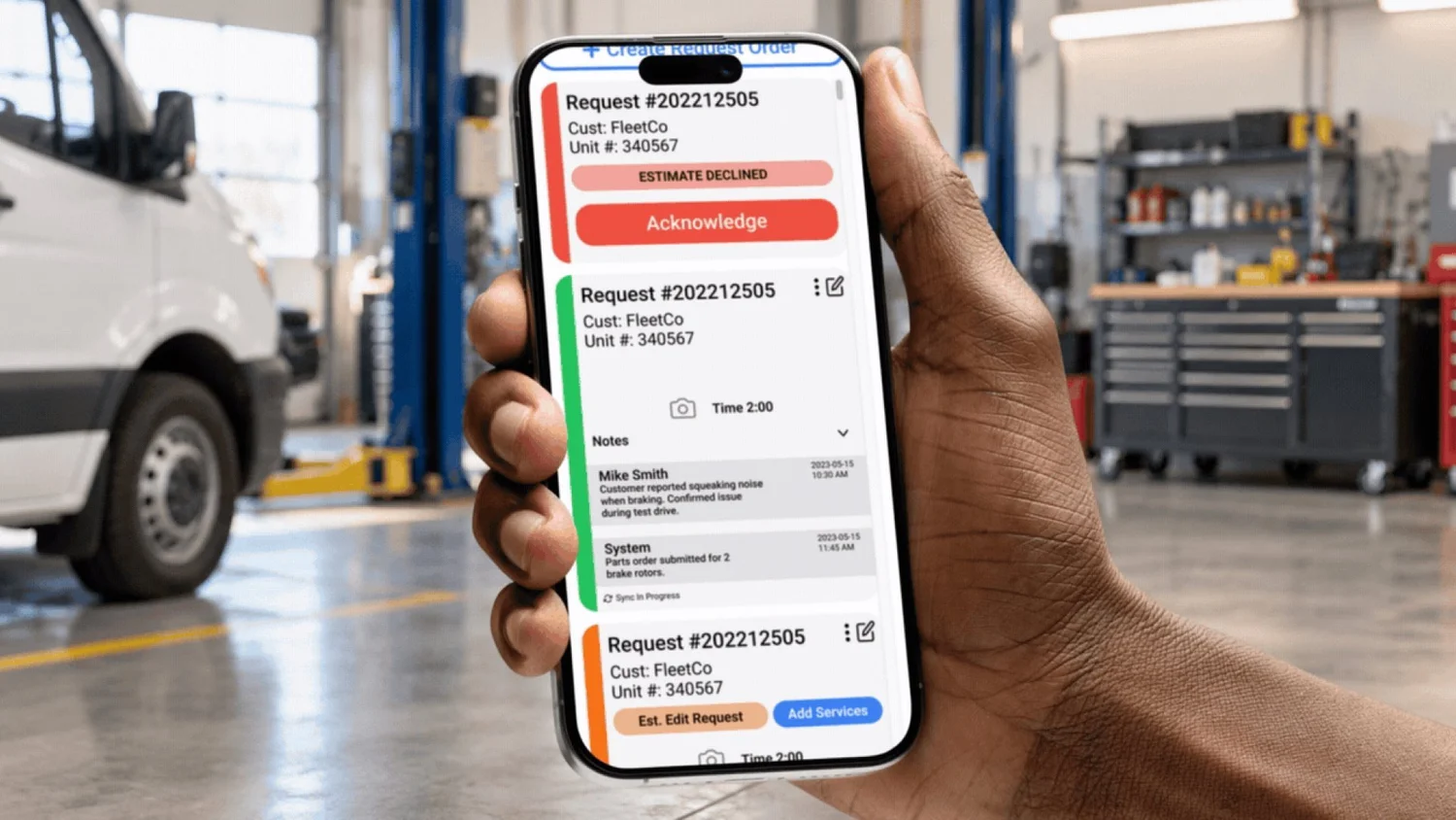 Mechanic's hand holding a phone showing the Fleet Mobile Maintenance app in a repair shop