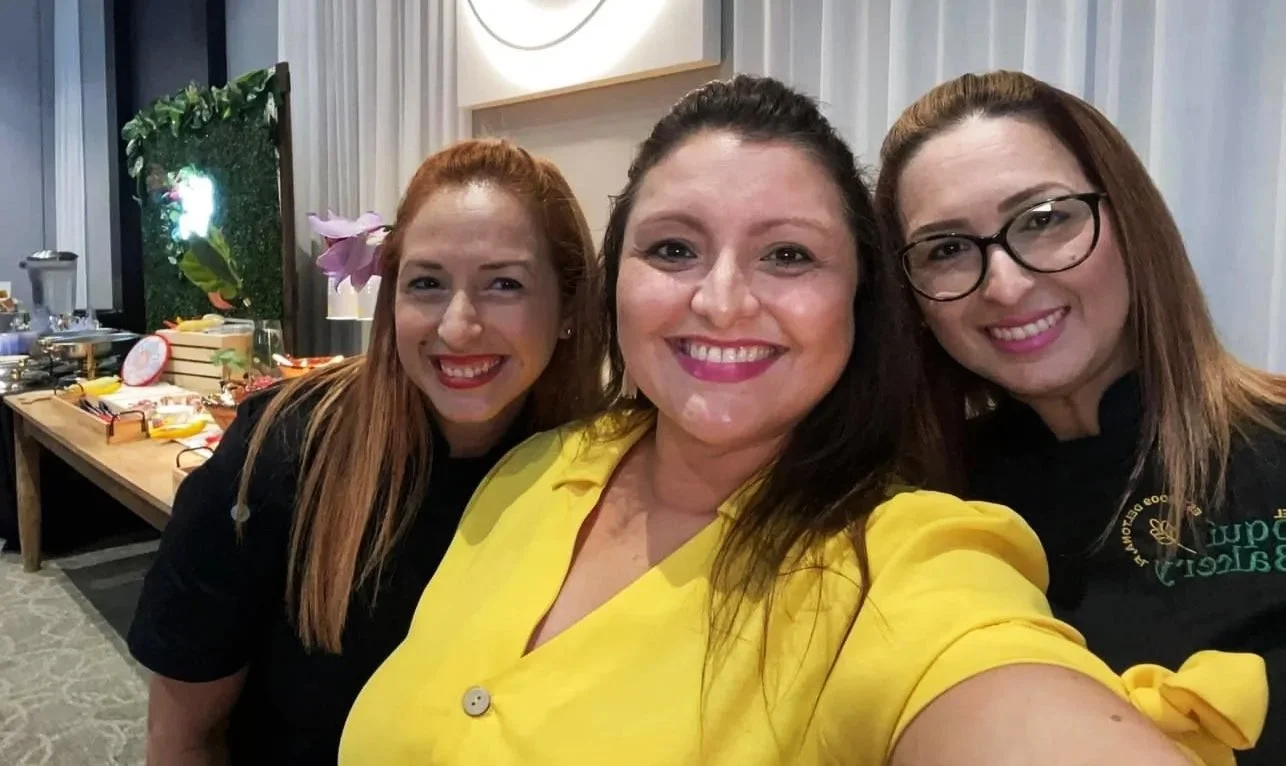 Three women taking a selfie at a social event, with a decorated table and food in the background.