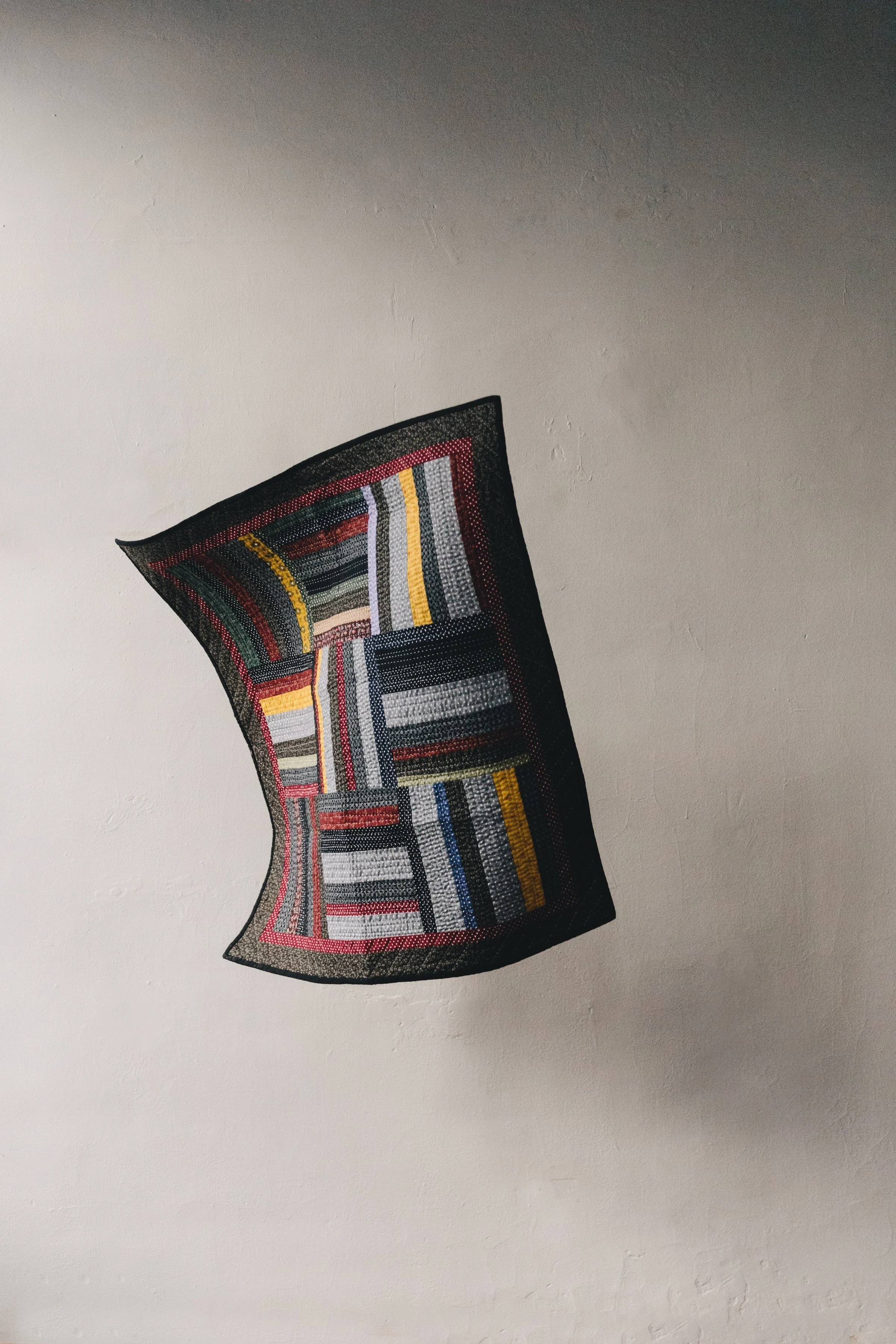 Colorful patchwork textile with geometric patterns on a textured wall background. Photographed in Ouseburn Studio
