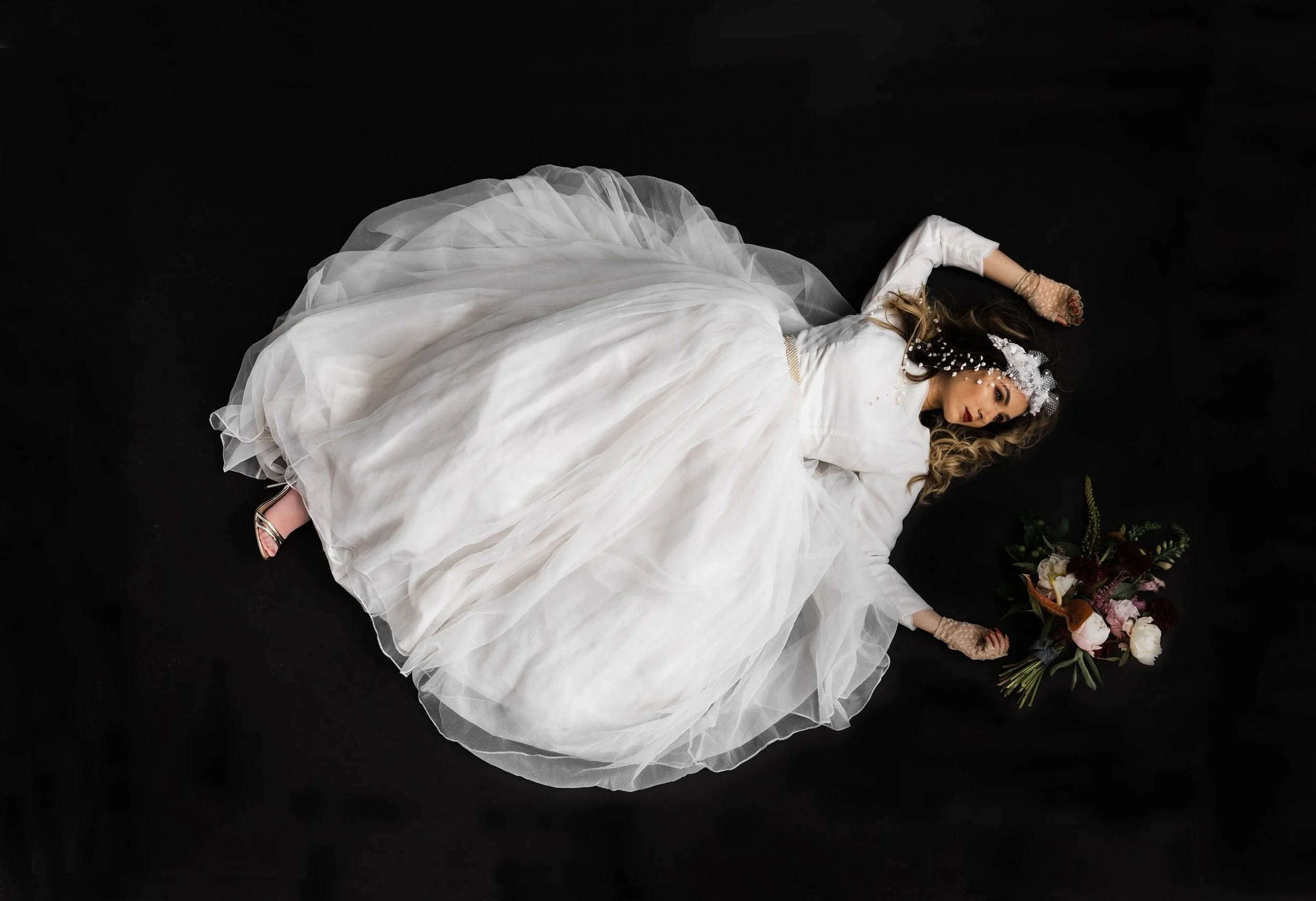 Bride lying on black background in white gown with bouquet