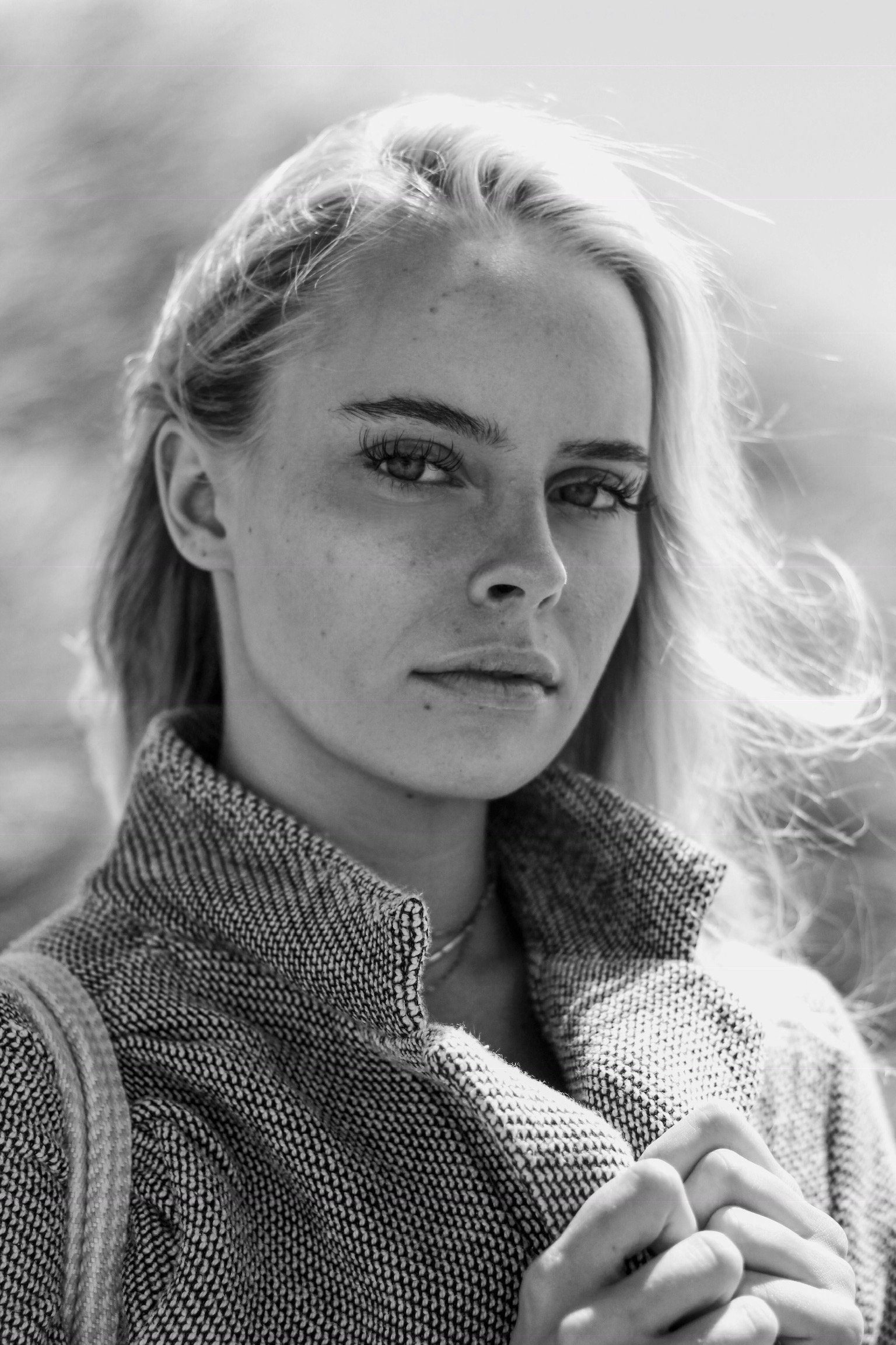 Black and white close-up portrait of a person with long hair wearing a checkered coat, looking directly at the camera.