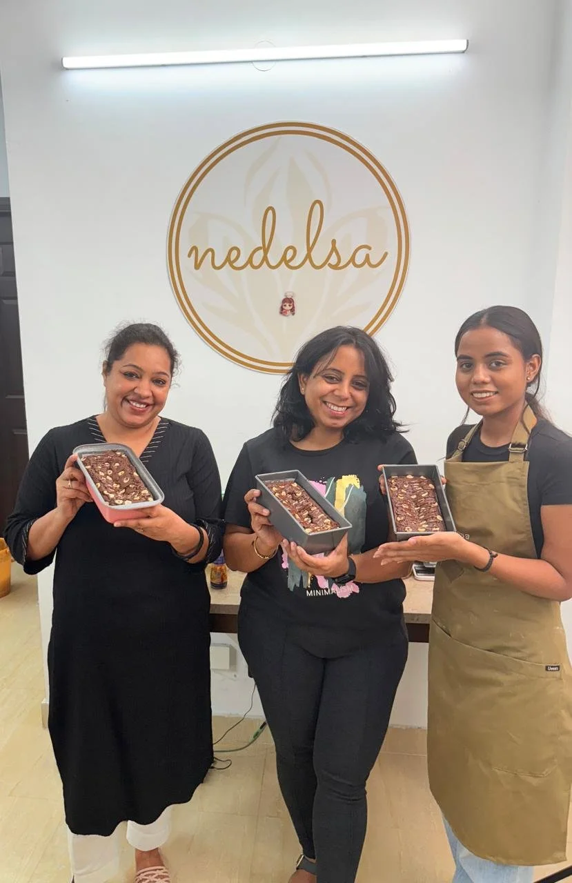Three women smiling and holding rectangular baking dishes with chocolate dessert, in front of a wall with 'Nedelsa' logo