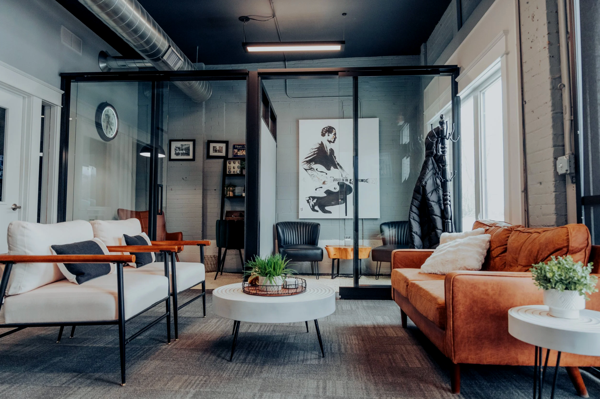 Modern office lounge with white and orange sofas, black chairs, potted plants, and wall art in the background.