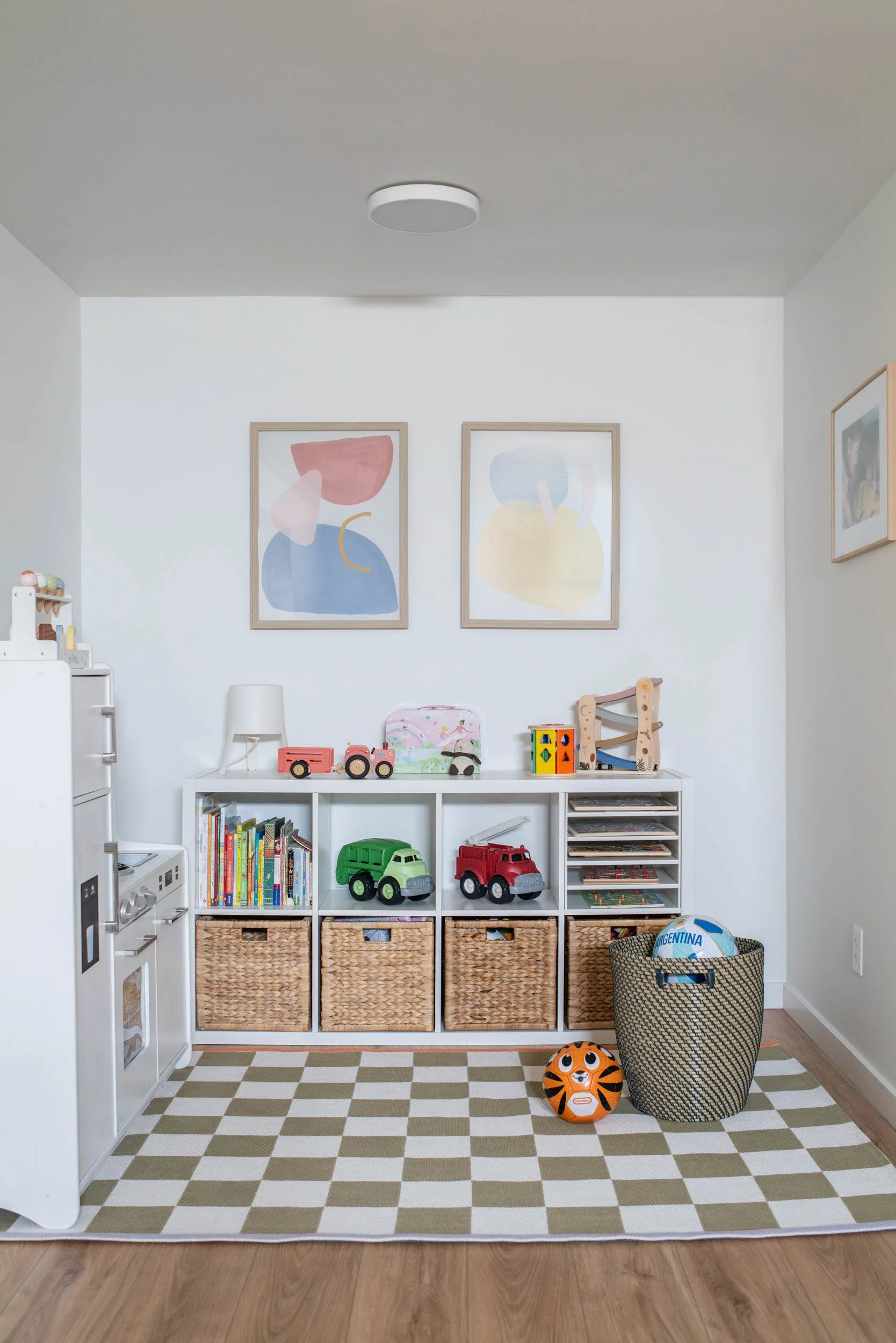 Basement playroom area with open cubbies for toys, play kitchen and playful checkered green and white rug