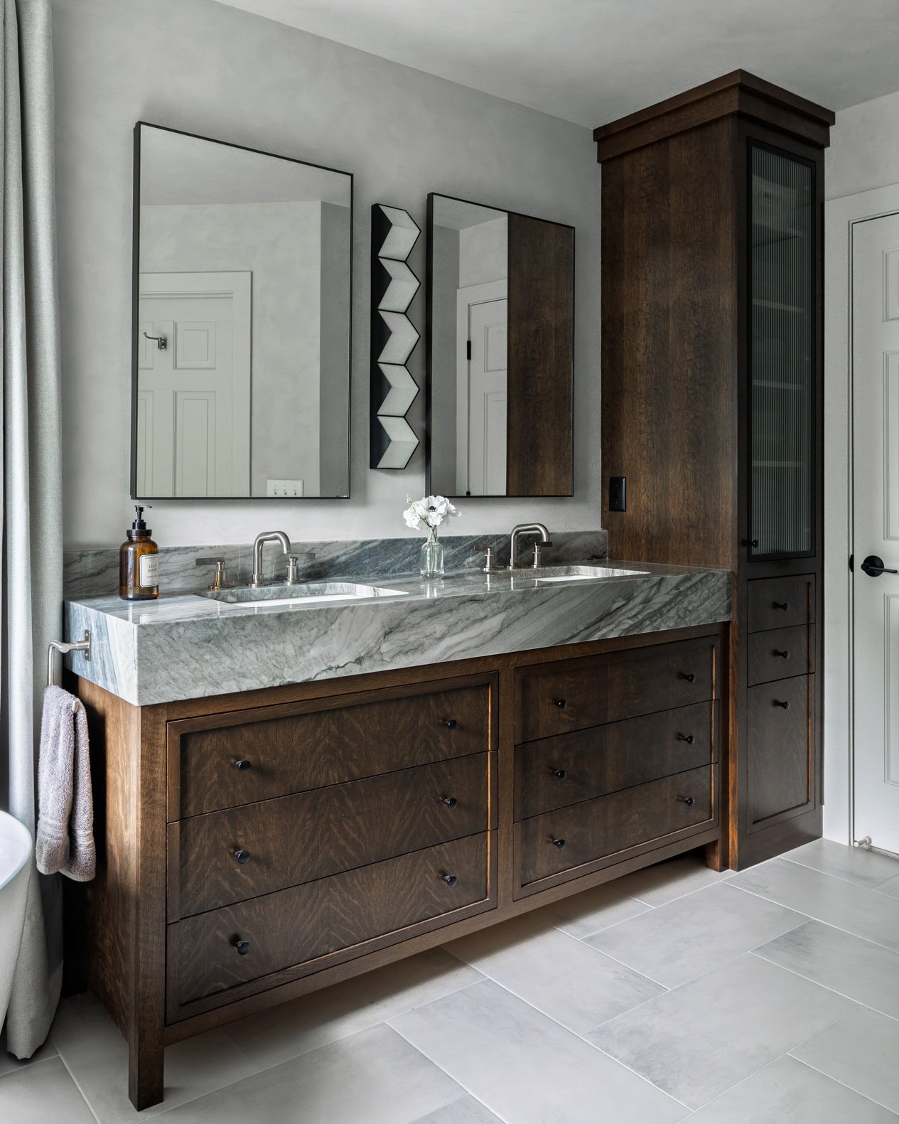 Luxurious and spacious master bathroom featuring a custom double vanity with a mitered edge countertop made from beautifully veined grey and white marble. The dark wood vanity cabinetry offers ample storage with multiple drawers and a rich, textured