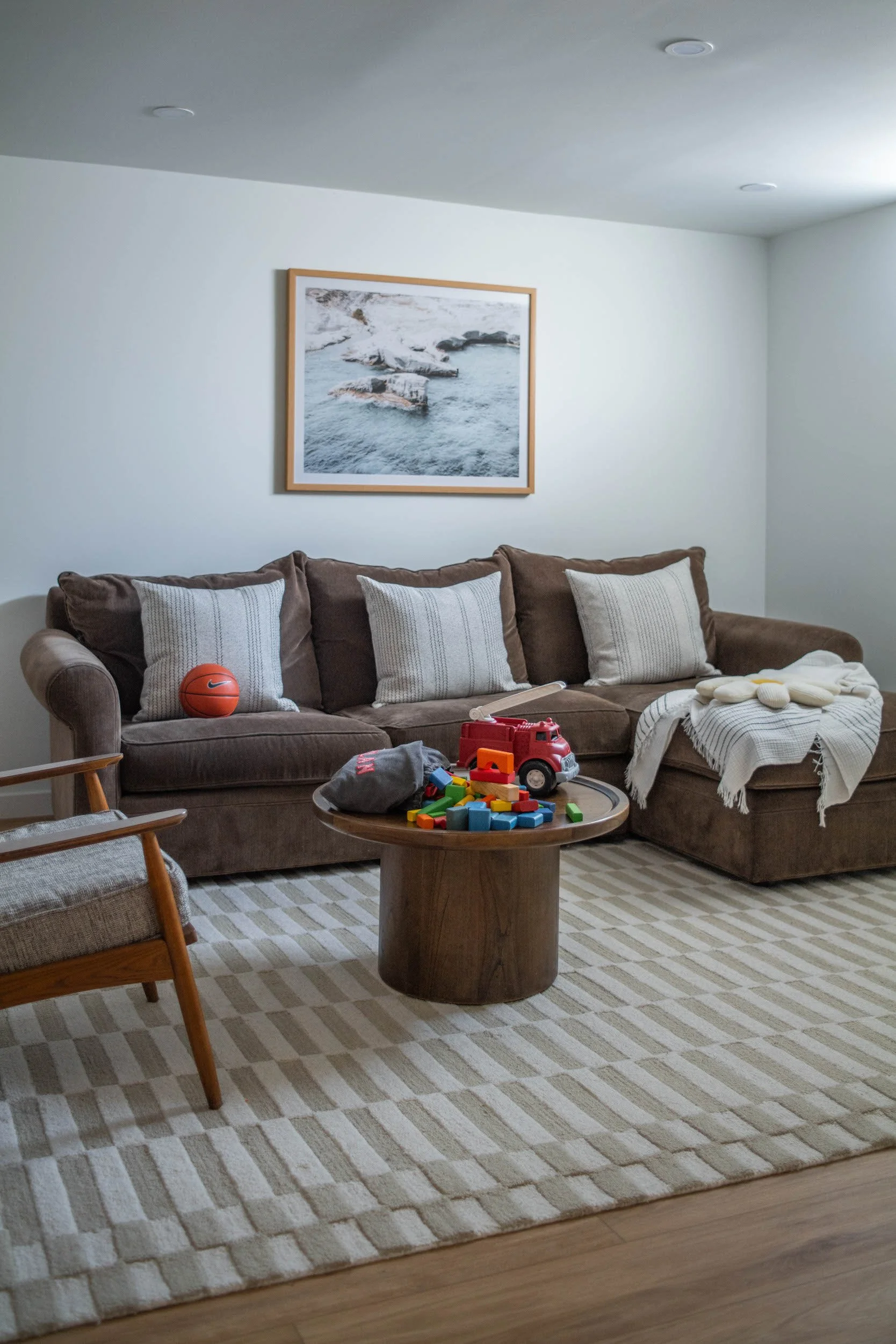 Basement family room with dark green sectional, round coffee table, mid-century modern accent chair and geometric design white and beige area rug