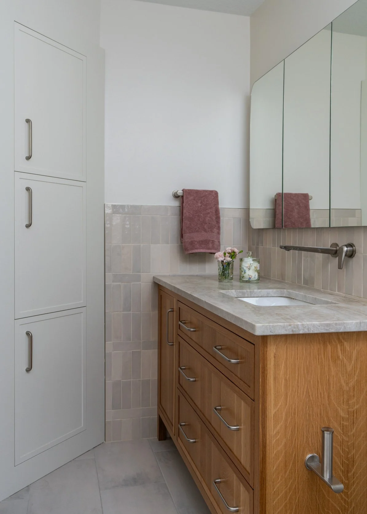 This image features a wonderful triple storage between studs. To the right a white oak vanity with a wall mounted faucet and a triple medicine cabinet above