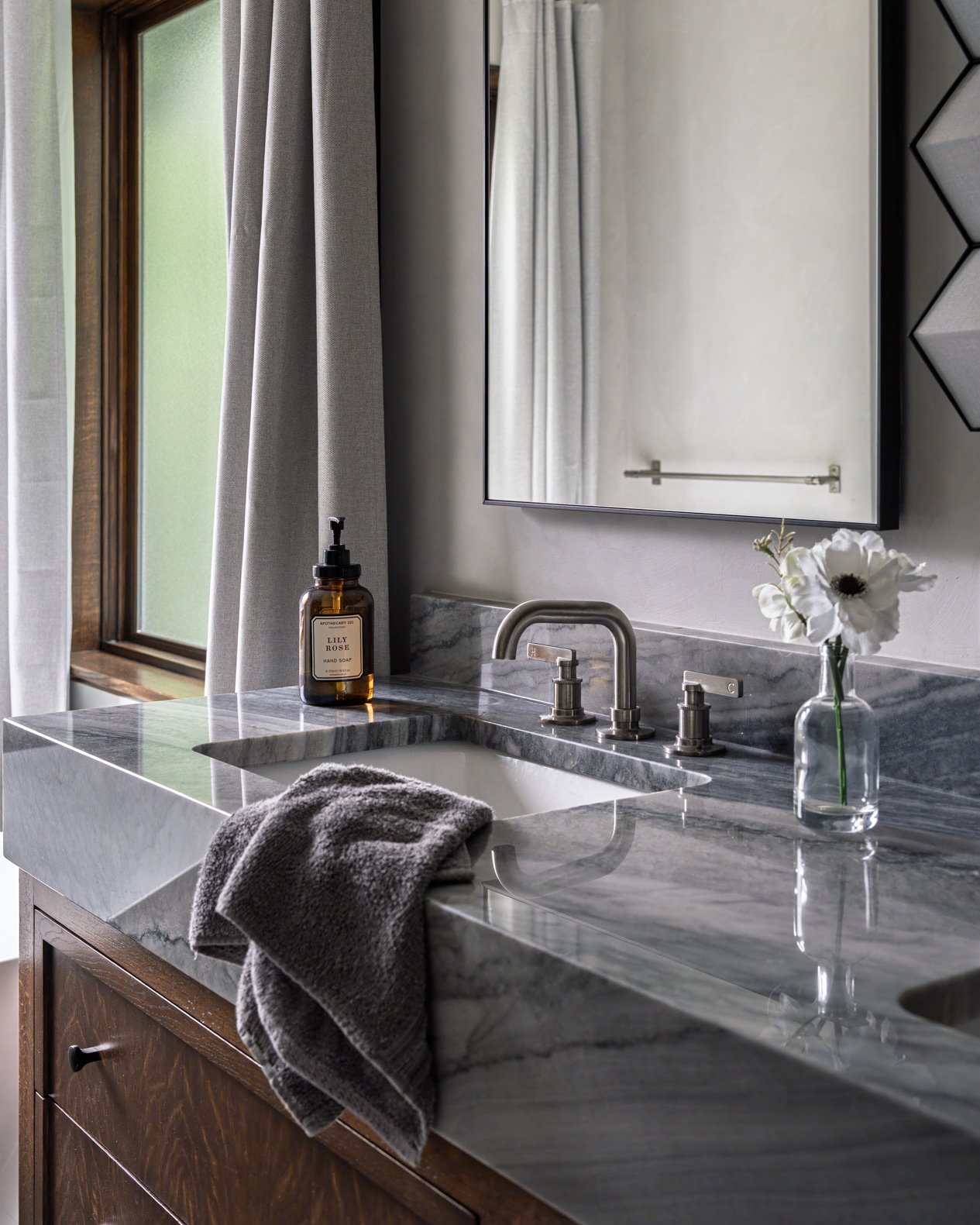 Stylish bathroom featuring a sleek quartz vanity countertop with sophisticated grey veining and an integrated sink. The modern design is complemented by a brushed nickel faucet and a wall-mounted mirror. A dark wood vanity with a simple pull adds war