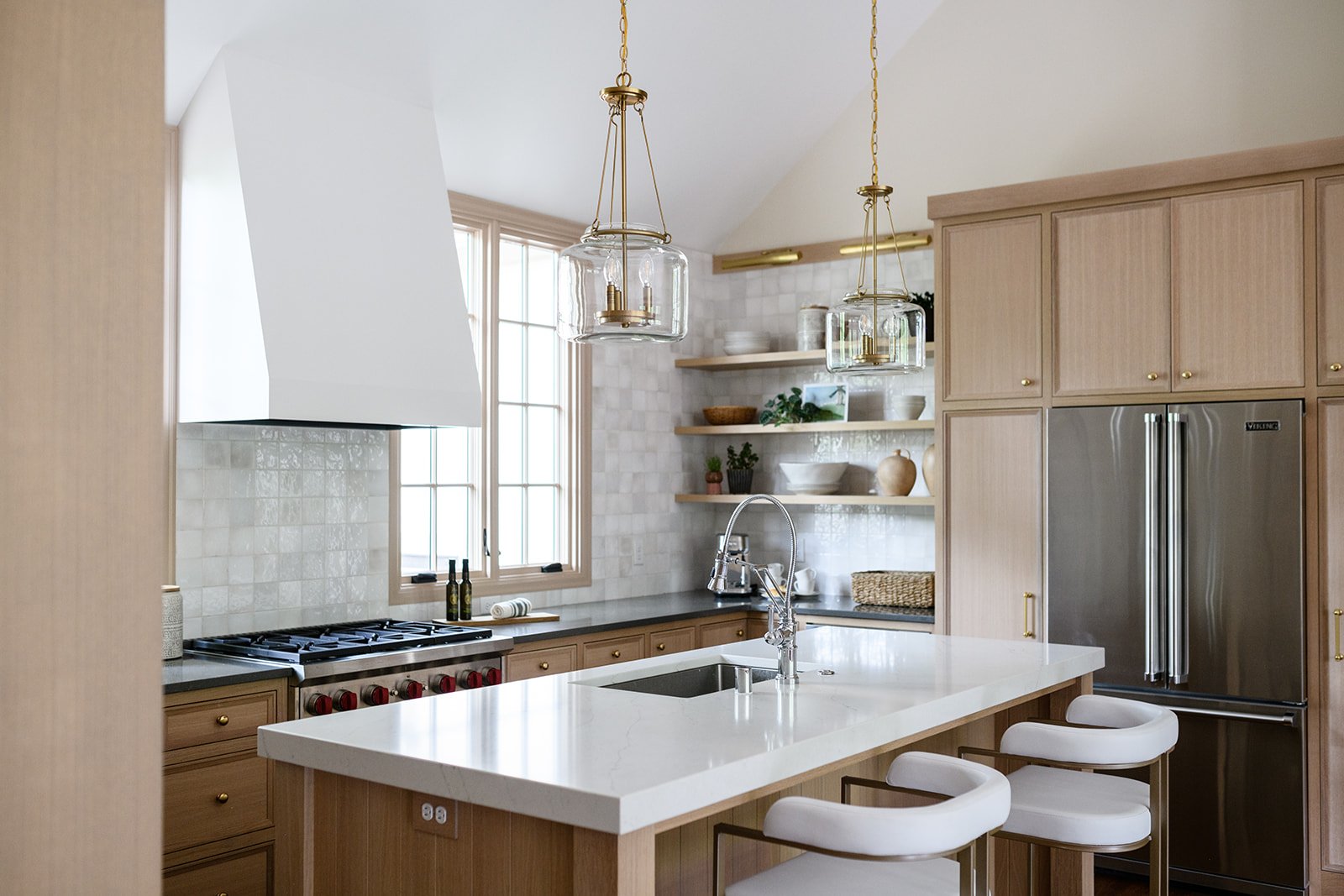 Symmetrical Lake of the Isles kitchen remodel featuring rift-cut white oak cabinets, large white quartz island with seating, brass pendants, and creamy zellige-look backsplash tile.