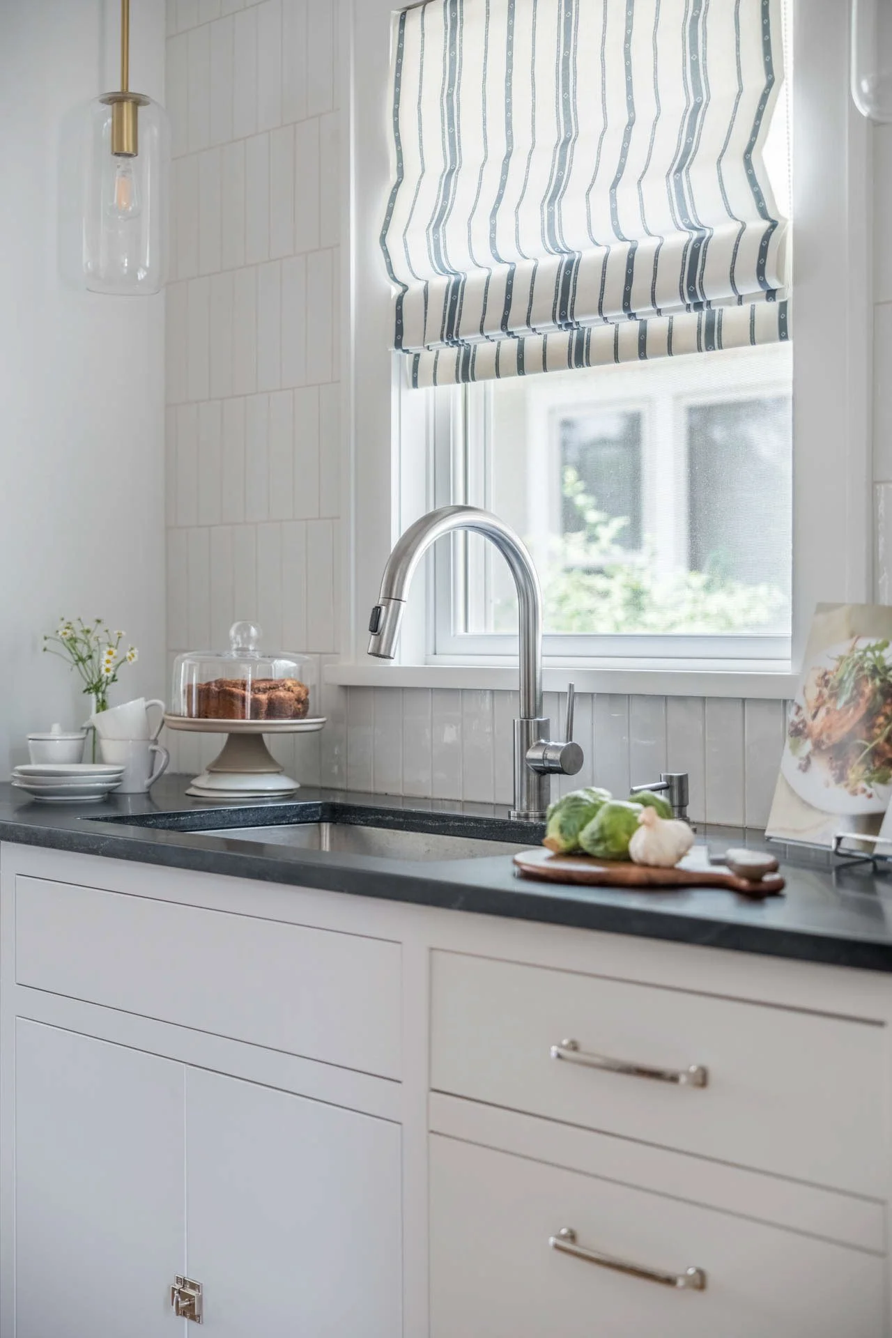 Kitchen featuring a striking black granite waterfall countertop, white perimeter cabinets, stainless steel refrigerator, and white subway tile backsplash.