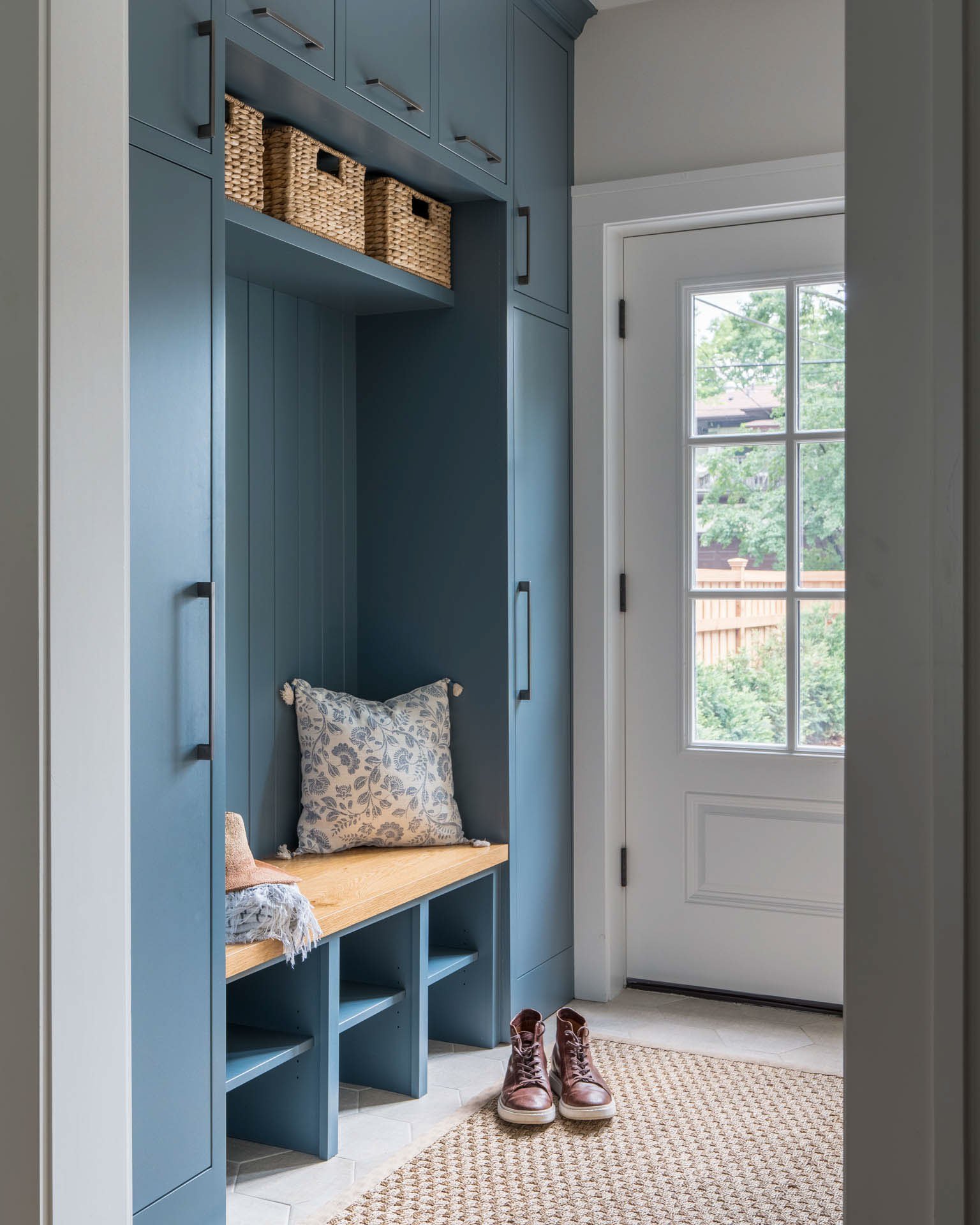 Custom blue built-in mudroom cabinetry with dark hardware, a white oak bench, and woven storage baskets in the Lynnhurst, Minneapolis remodel.