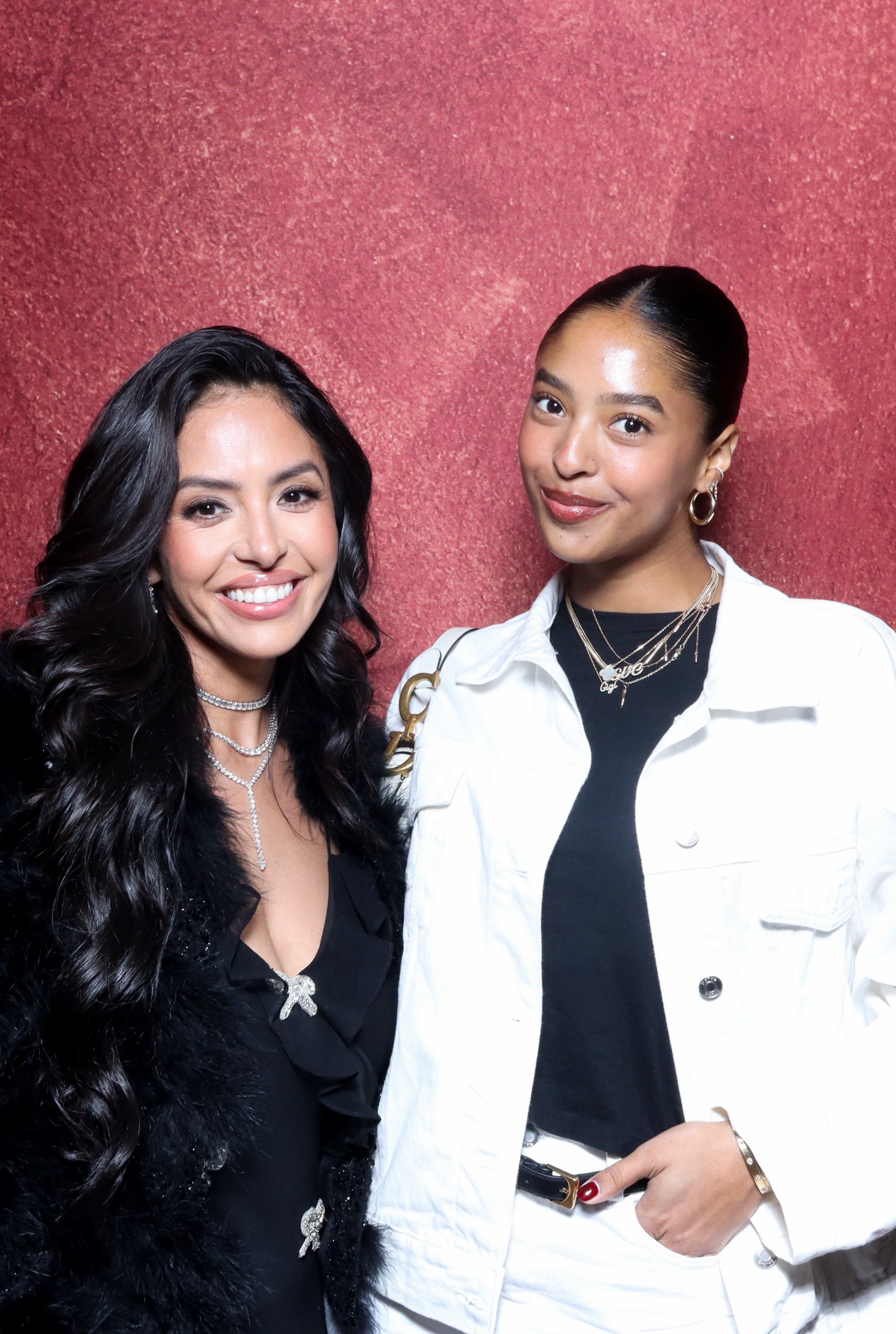Two women standing together against a red background, smiling at the camera.