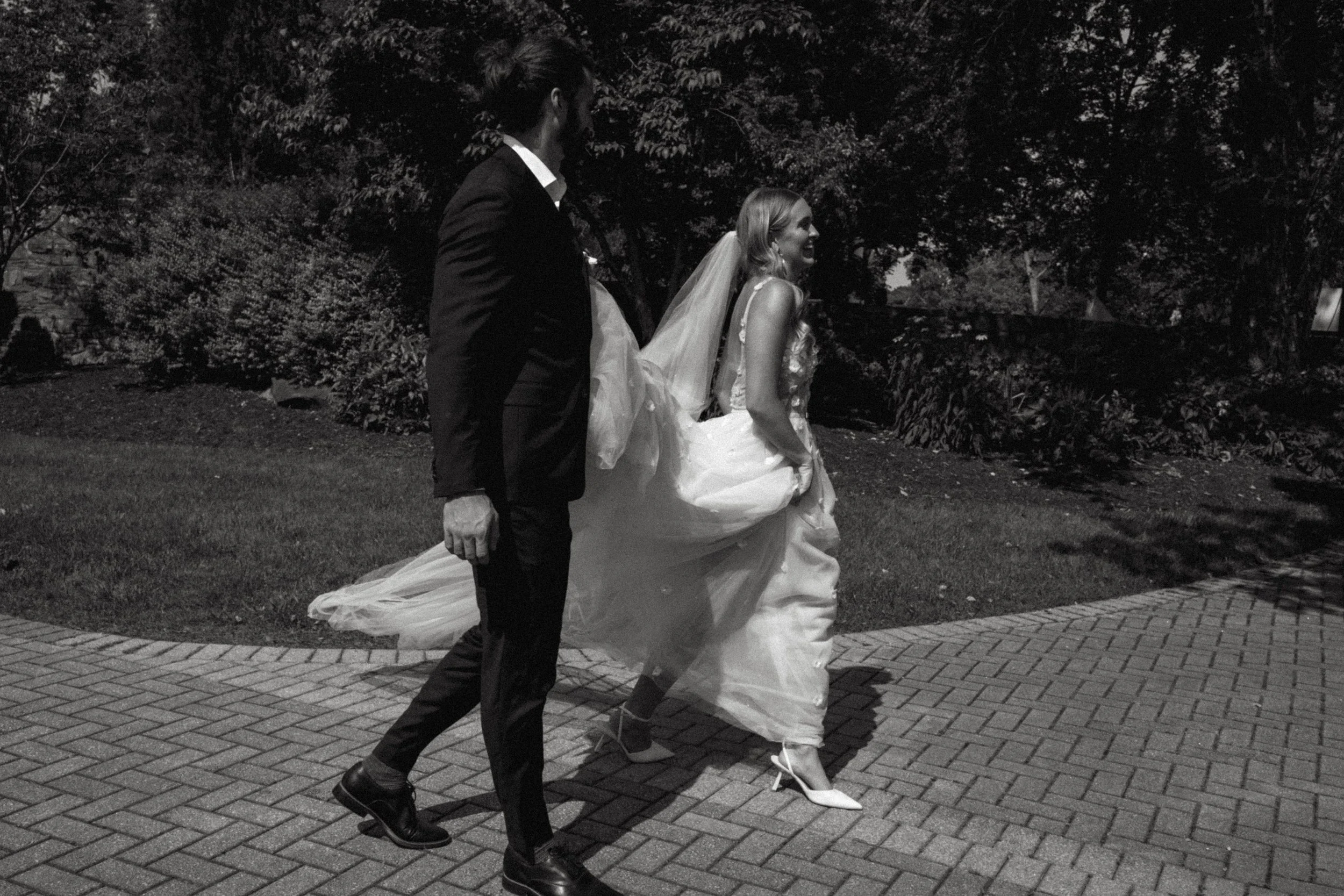 A woman in a wedding dress and a groom in a suit walking on a brick path outdoors at night.