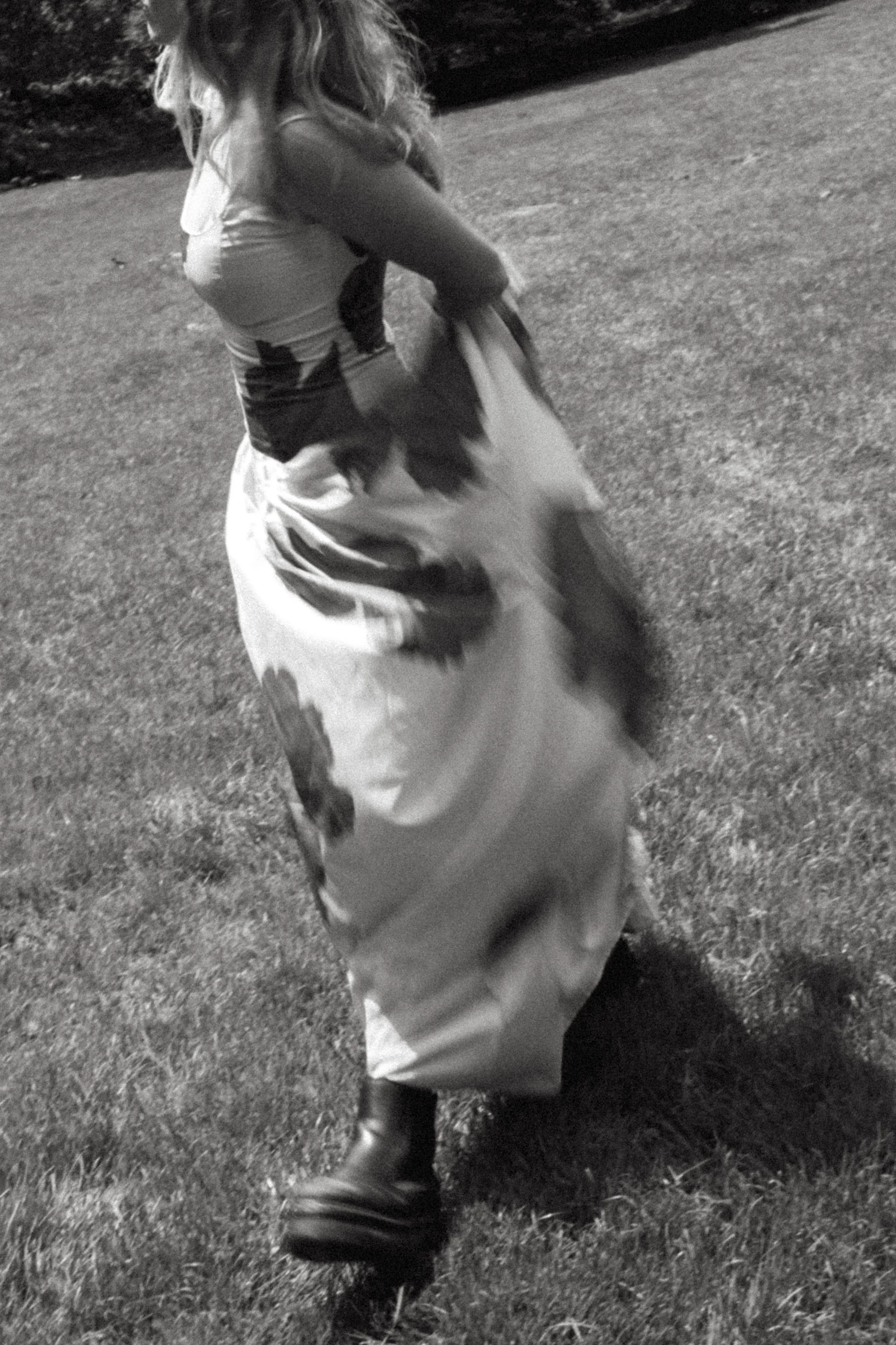 A person wearing a flowing dress and boots walking on grass, with their face not visible.