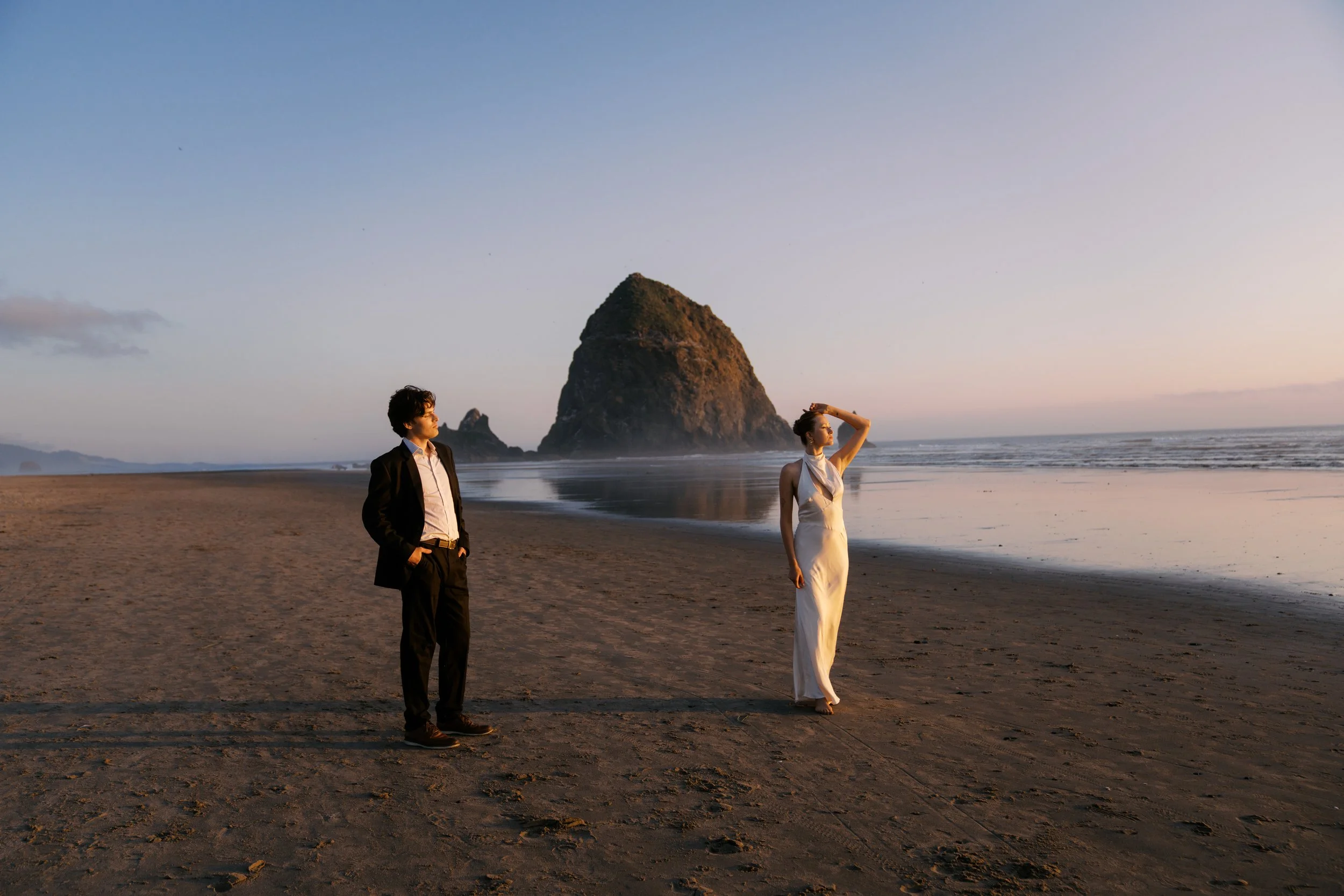 Bride and groom on their wedding elopement day on the beach during sunset. The groom looks at his bride who is standing distanced from him, looking out at the ocean on the east coast.