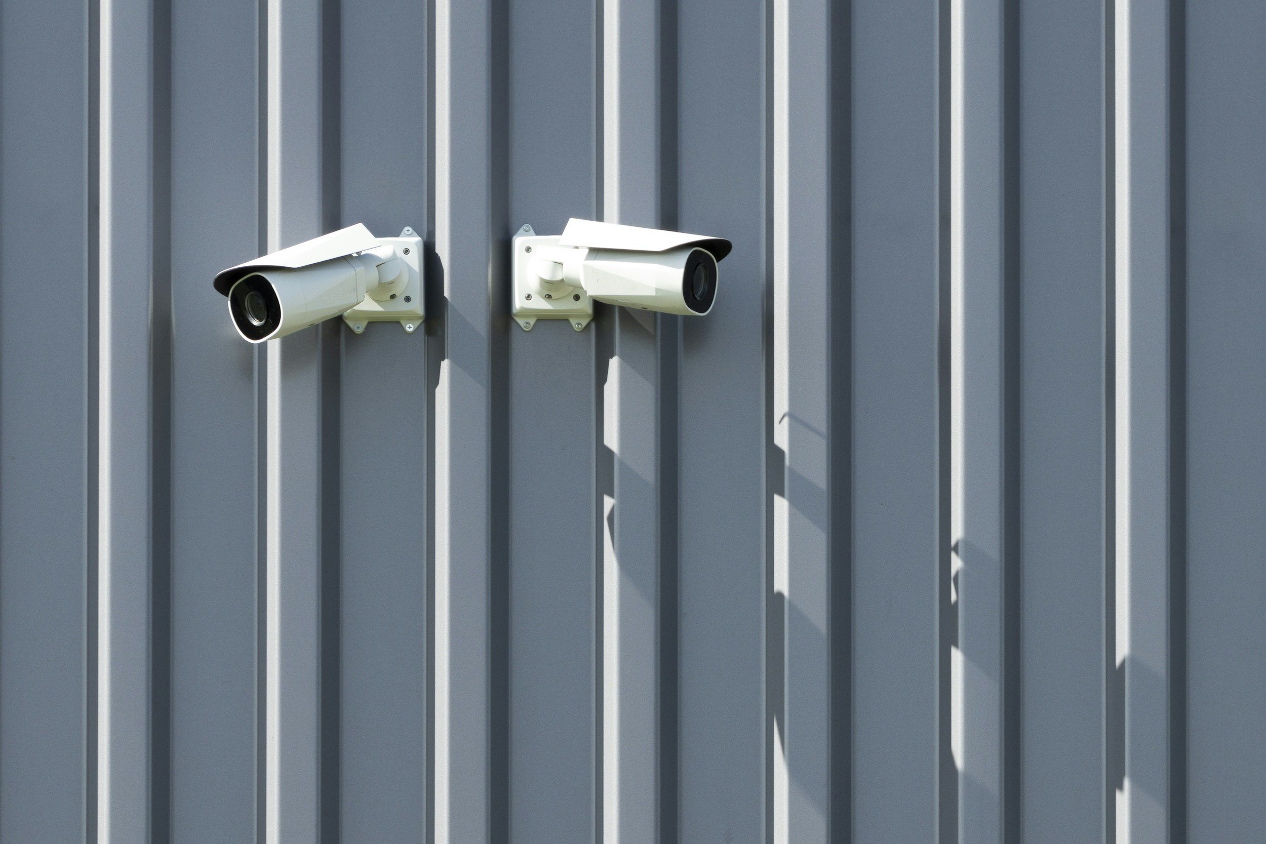 Two security cameras mounted on a gray metal wall.