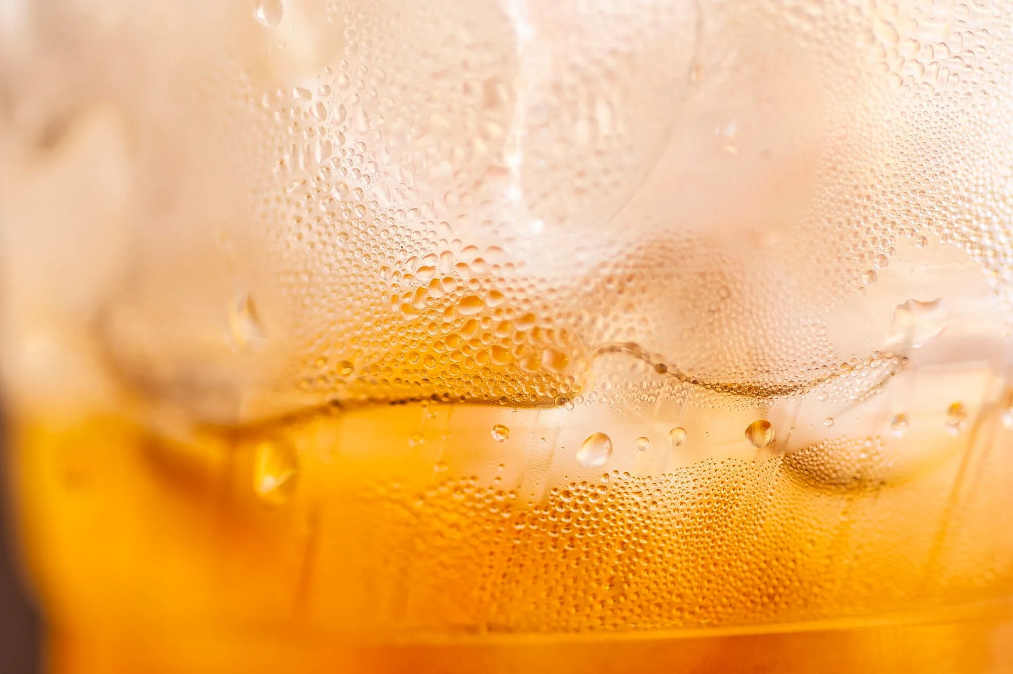 Close-up of a cold glass with condensation and bubbles, filled with a golden-colored beverage.