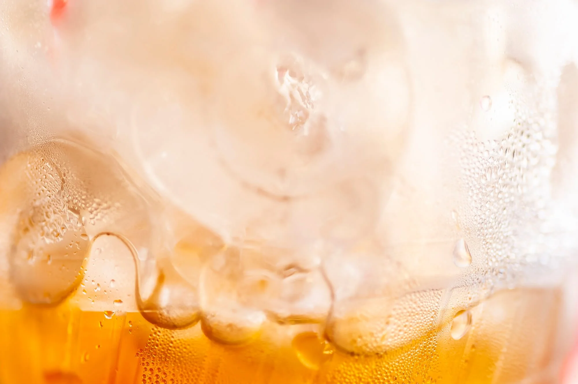 Close-up of a glass with ice cubes and a golden-colored beverage with condensation on the outside.