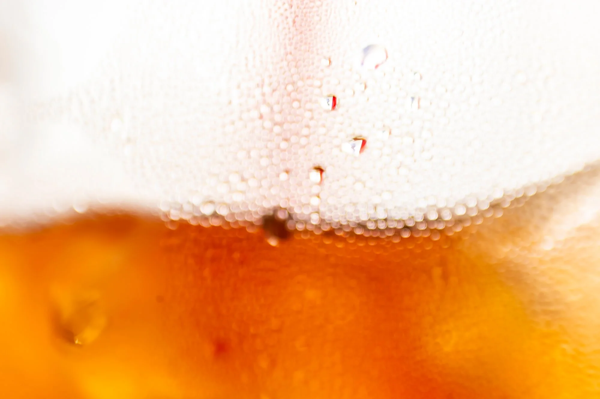 Close-up of a glass of beer with foam at the top and condensation droplets on the surface.