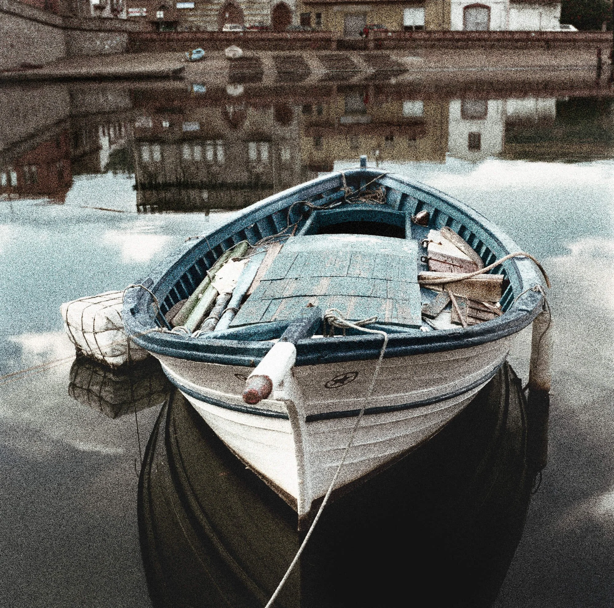 A small blue and white wooden boat floats on calm water with buildings reflected in the background.